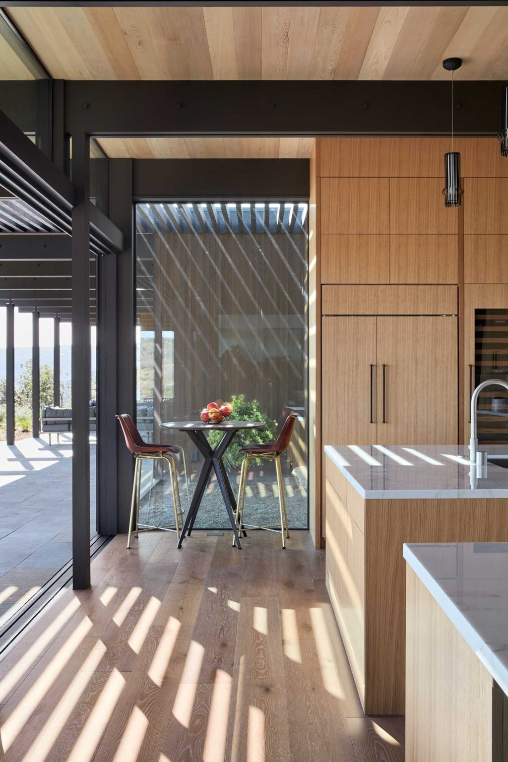 A continuous wood wall links the entry and kitchen, where tall cabinetry, pendant lighting, and light counters create a welcoming space.