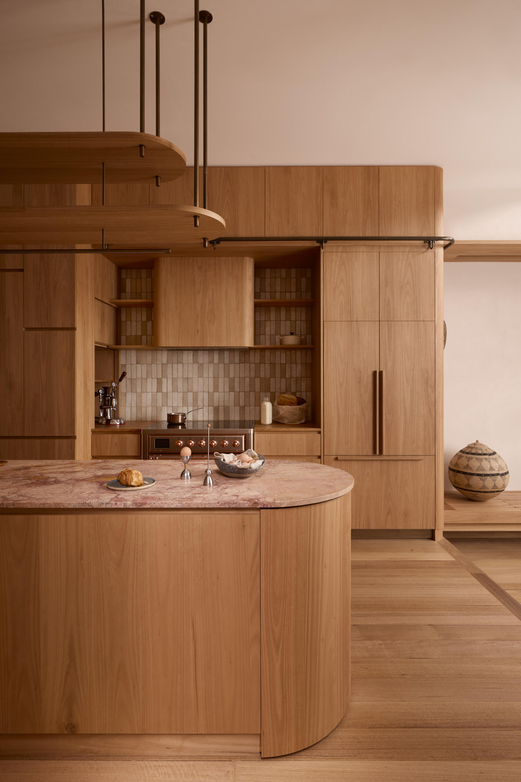 The kitchen forms the center of the home. Timber joinery, blush stone, handmade tiles, and copper detailing come together in a composition that feels tactile and expressive. It operates as both cooking space and social hub, opening directly to the lounge.