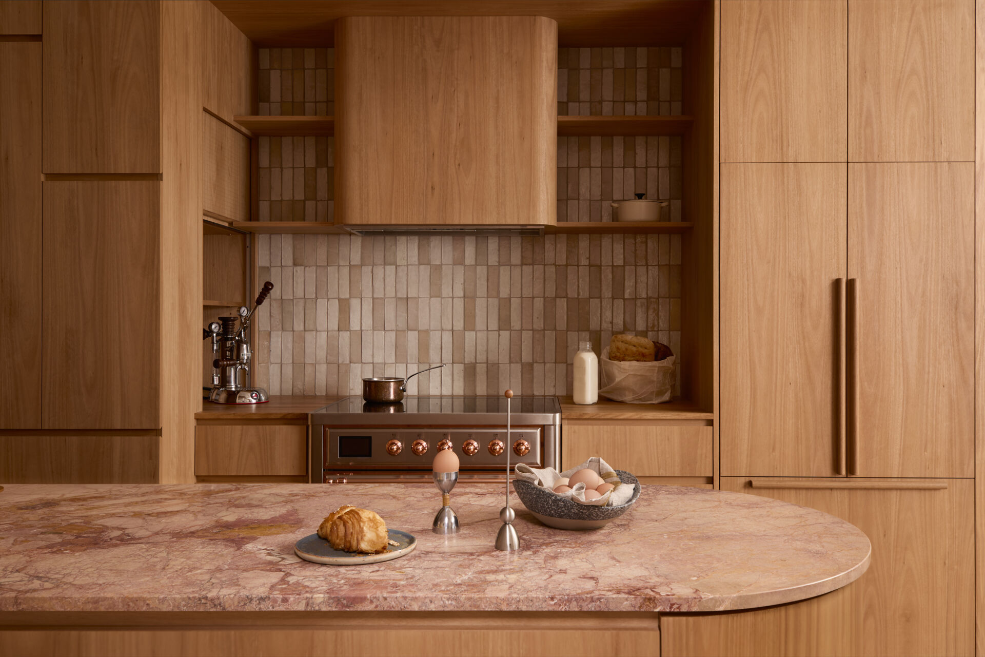 The kitchen forms the center of the home. Timber joinery, blush stone, handmade tiles, and copper detailing come together in a composition that feels tactile and expressive. It operates as both cooking space and social hub, opening directly to the lounge.