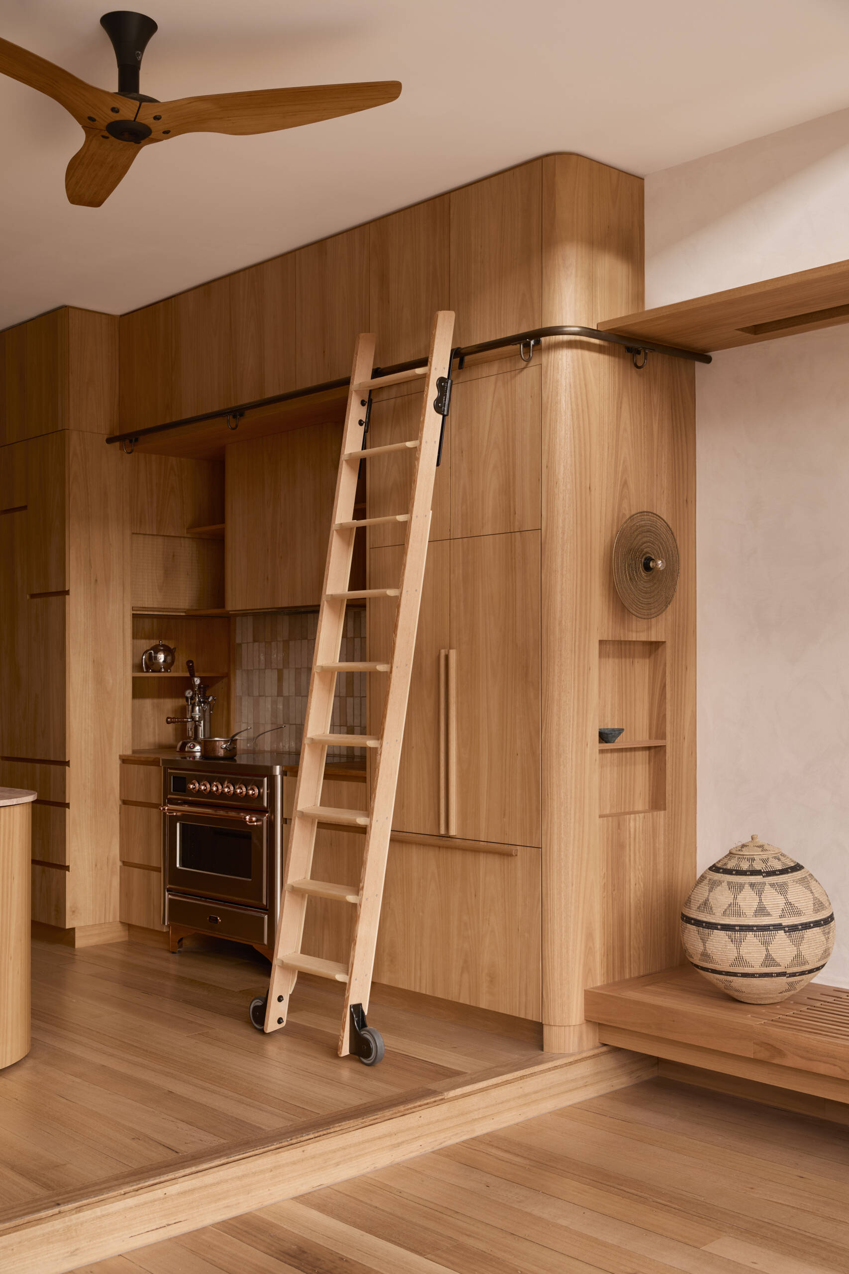 The kitchen forms the center of the home. Timber joinery, blush stone, handmade tiles, and copper detailing come together in a composition that feels tactile and expressive. It operates as both cooking space and social hub, opening directly to the lounge.