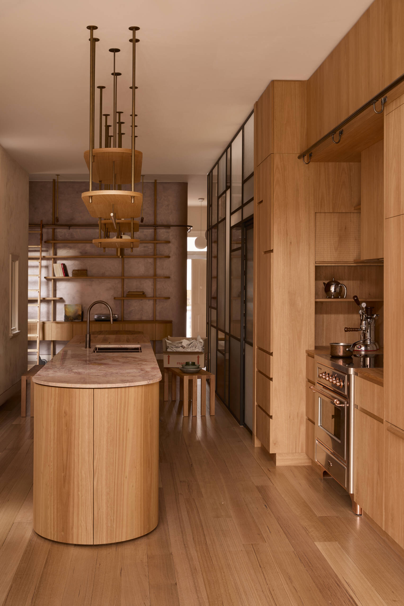 The kitchen forms the center of the home. Timber joinery, blush stone, handmade tiles, and copper detailing come together in a composition that feels tactile and expressive. It operates as both cooking space and social hub, opening directly to the lounge.
