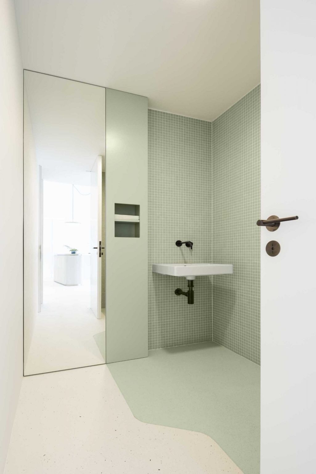 Hidden behind a simple white door, the bathroom continues the clinic's signature green palette with tiled walls and clean minimalist detailing.