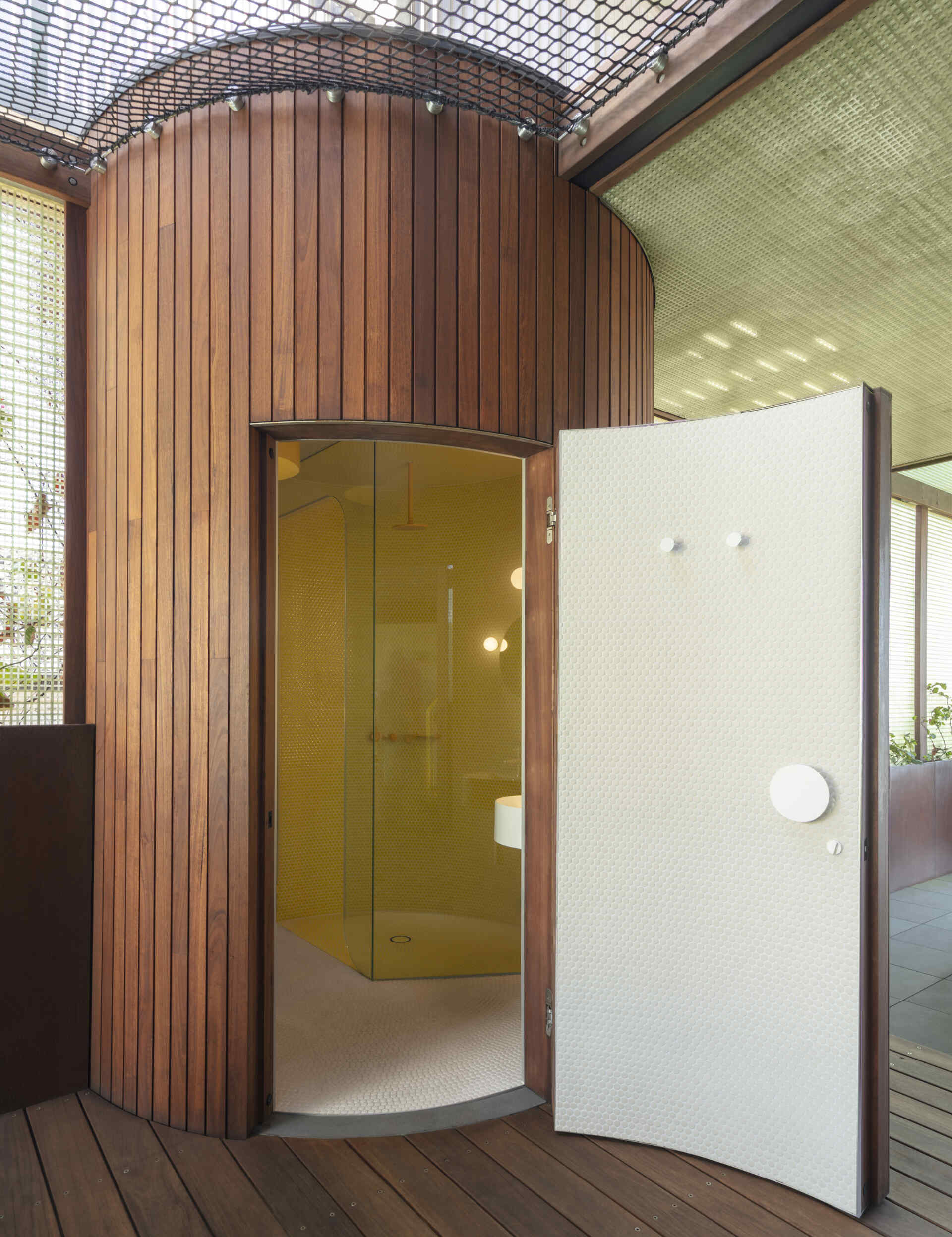 A secret steam room hidden behind a curved door features yellow penny tiles, a circular skylight, and playful architectural details.