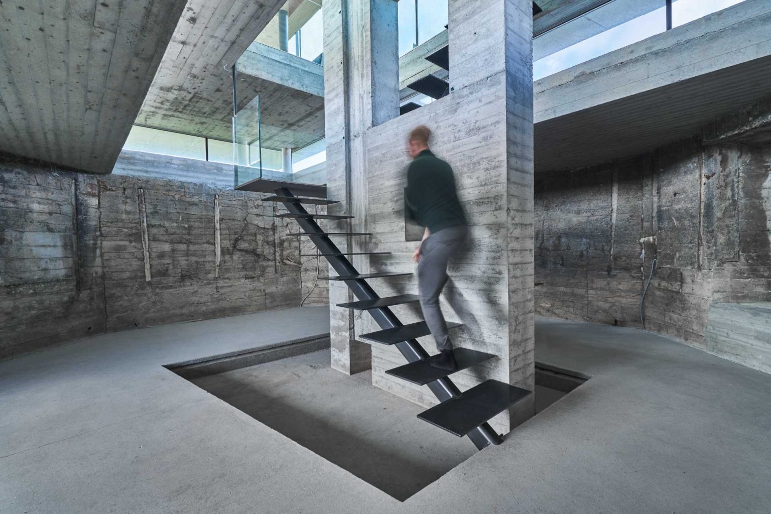 A staircase transforms the journey through this renovated bunker, leading visitors from solid concrete interiors into a bright glass pavilion above.