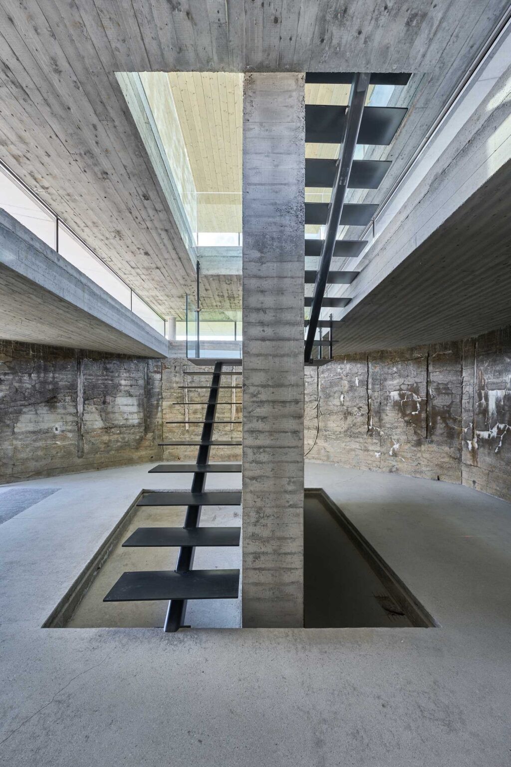 A staircase transforms the journey through this renovated bunker, leading visitors from solid concrete interiors into a bright glass pavilion above.