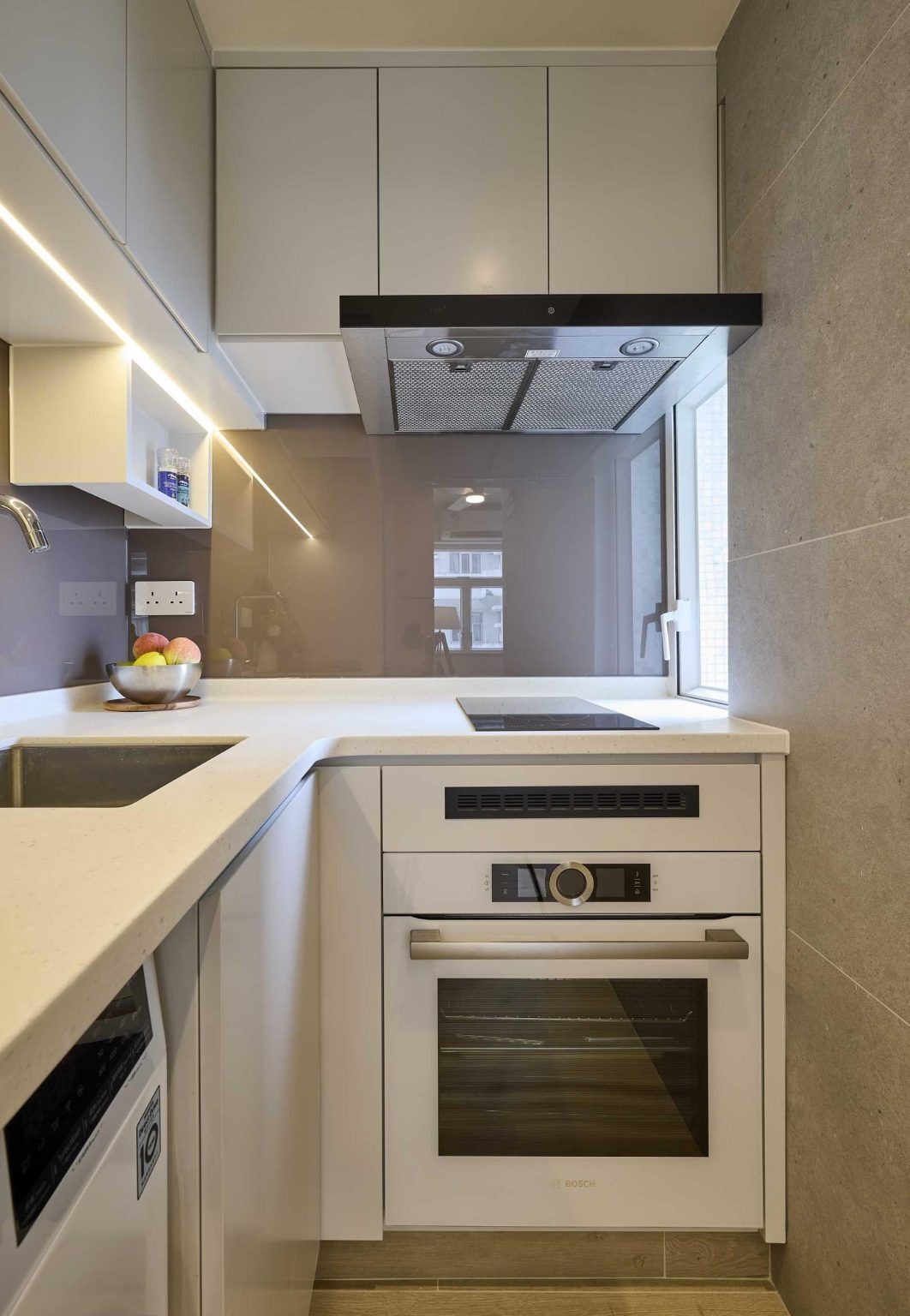 Tucked into an alcove, this minimalist kitchen combines white cabinetry, a grey backsplash, and integrated appliances for a clean and efficient design.