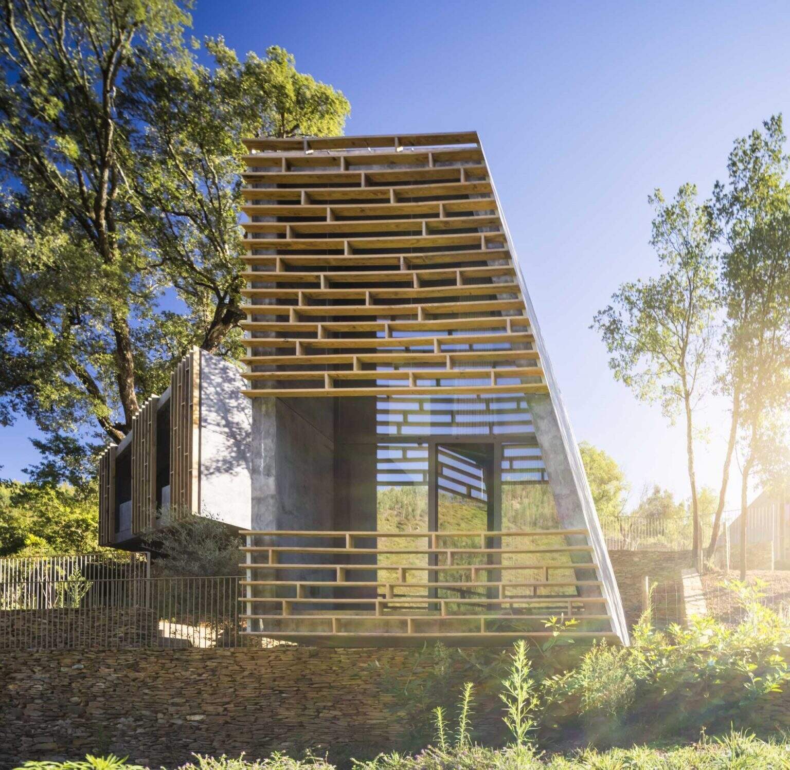 Raw concrete structures paired with vertical timber screens give these forest cabins a distinctive contemporary appearance. The timber elements provide privacy, shade, and filtered views while helping the buildings blend into the landscape.