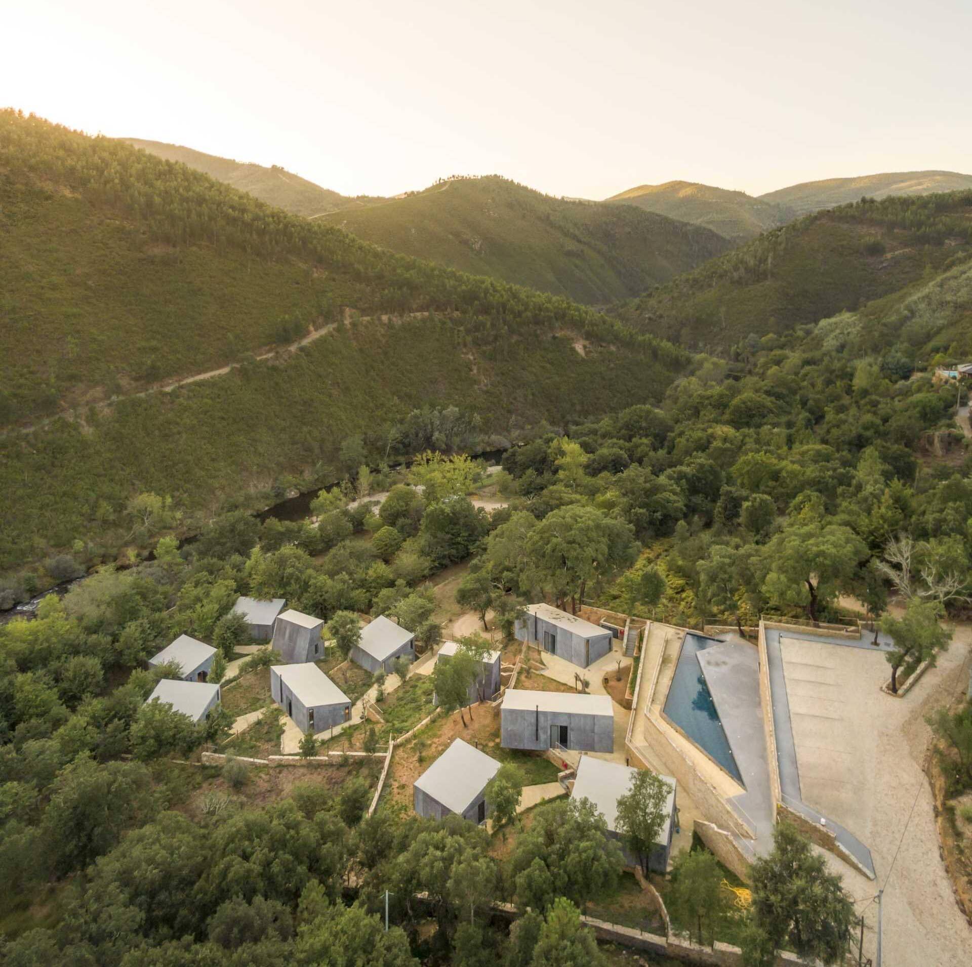 Eleven cabins in four unique designs are scattered across a Portuguese forest, preserving existing stone walls and mature trees. Their layout allows every home to enjoy open views of the surrounding woodland and river.