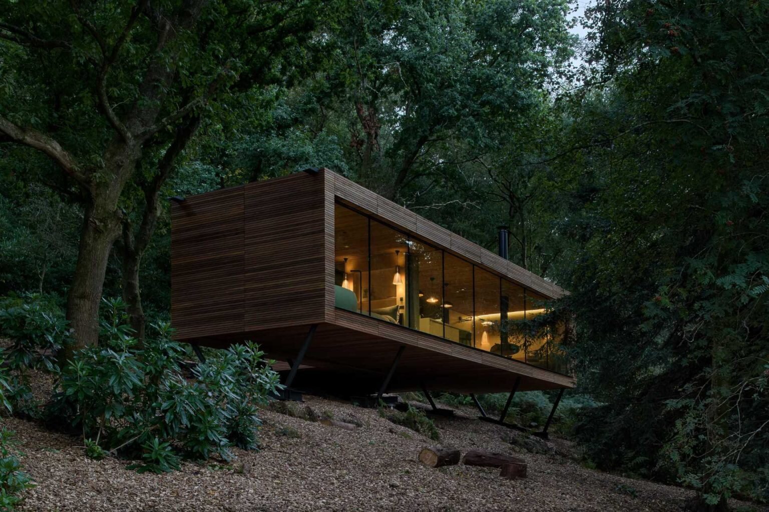 As night falls, this cedar lodge softly glows through the trees while remaining respectful of the surrounding protected landscape.