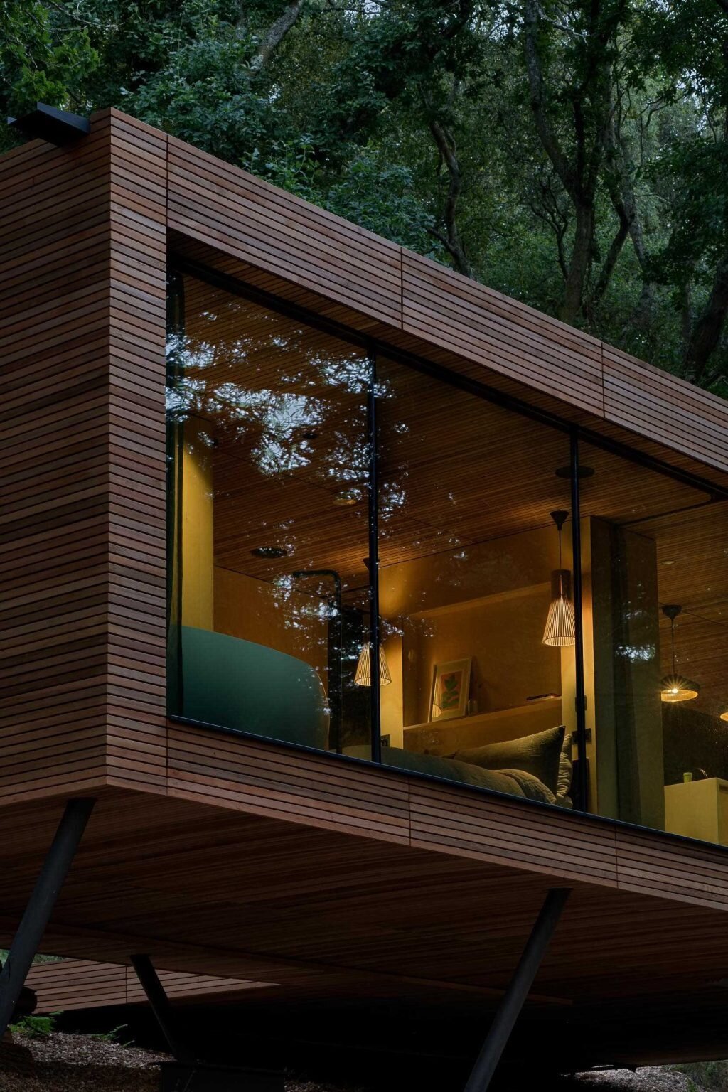 As night falls, this cedar lodge softly glows through the trees while remaining respectful of the surrounding protected landscape.