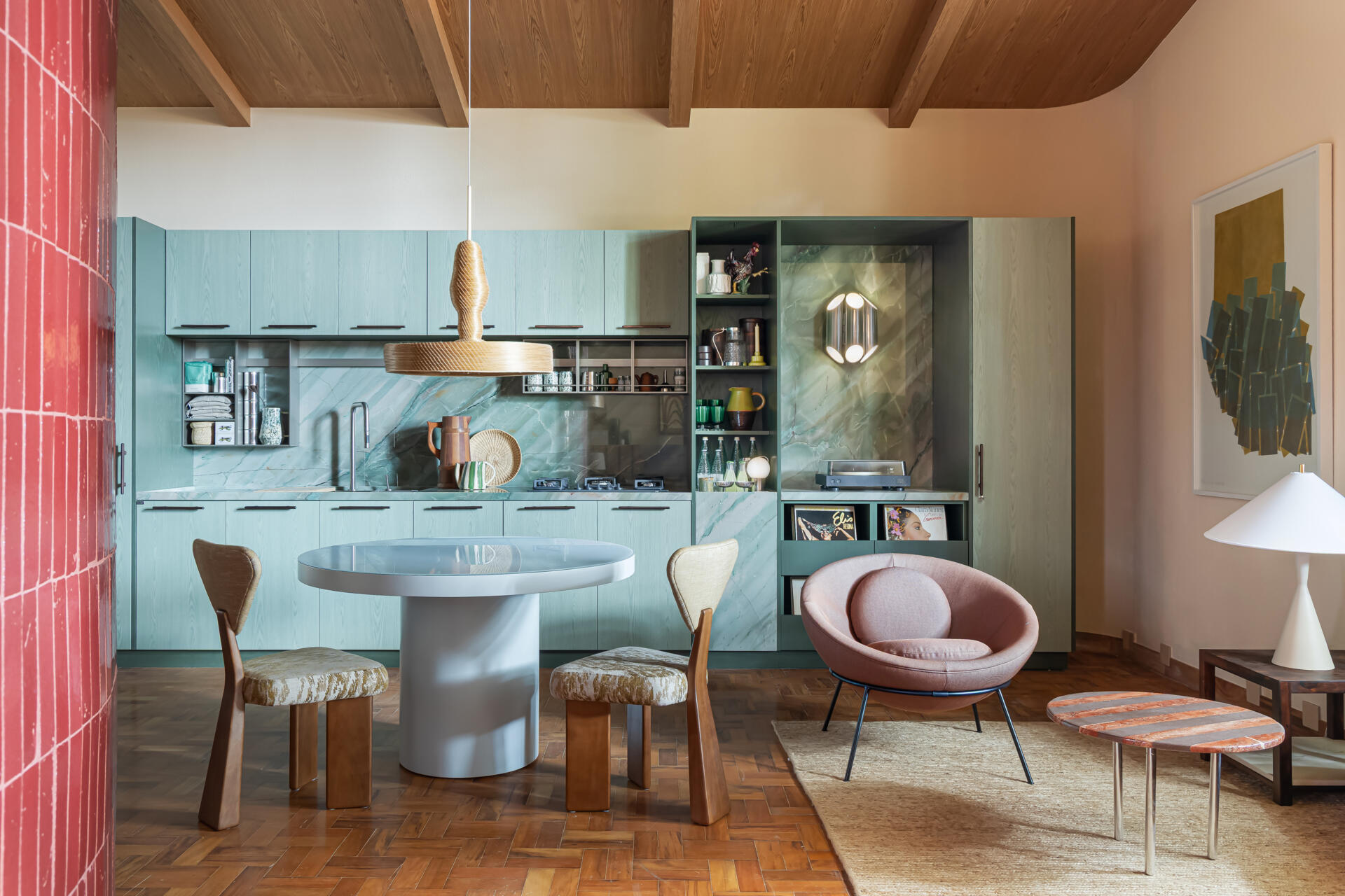This kitchen and dining space combines green-toned cabinetry, quartzite surfaces, handcrafted lighting, and Brazilian design pieces in a stylish social setting.