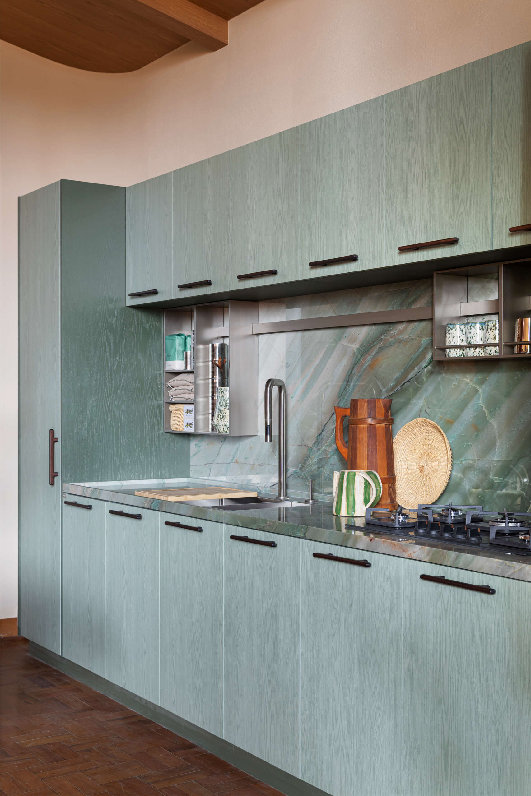 This kitchen and dining space combines green-toned cabinetry, quartzite surfaces, handcrafted lighting, and Brazilian design pieces in a stylish social setting.