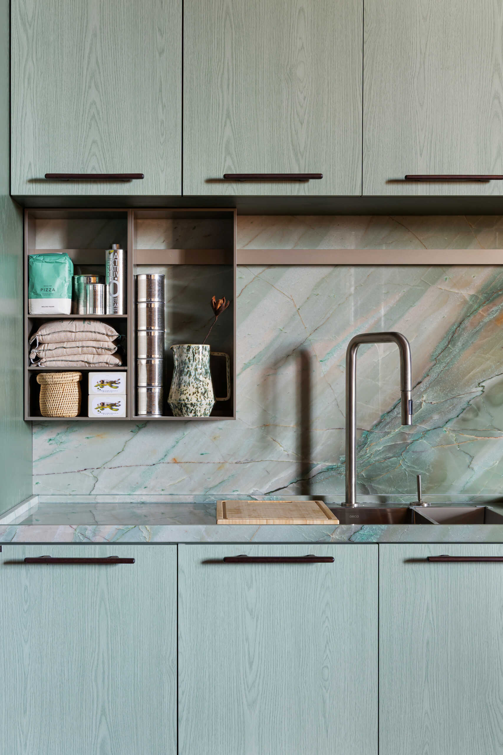 This kitchen and dining space combines green-toned cabinetry, quartzite surfaces, handcrafted lighting, and Brazilian design pieces in a stylish social setting.