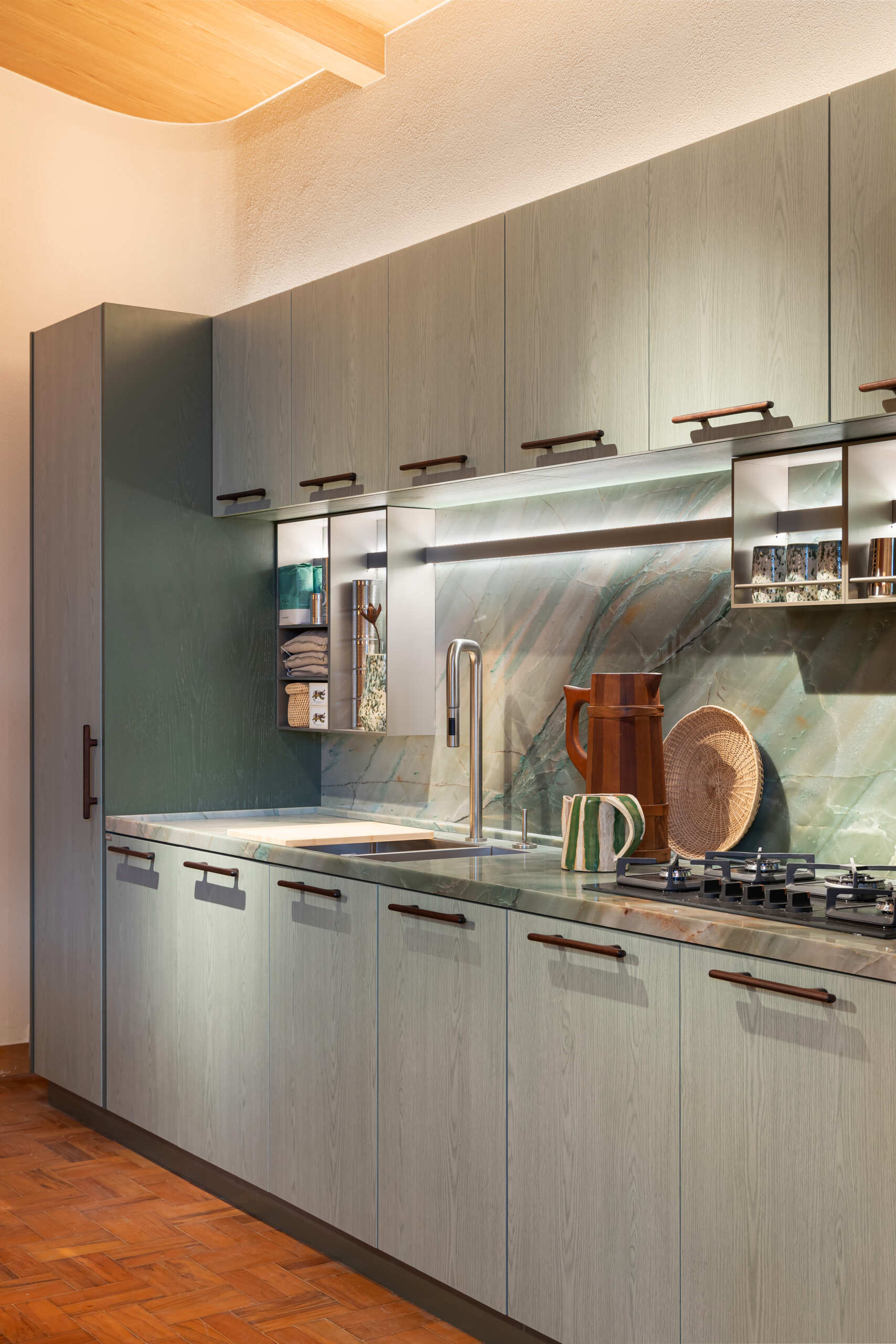 This kitchen and dining space combines green-toned cabinetry, quartzite surfaces, handcrafted lighting, and Brazilian design pieces in a stylish social setting.