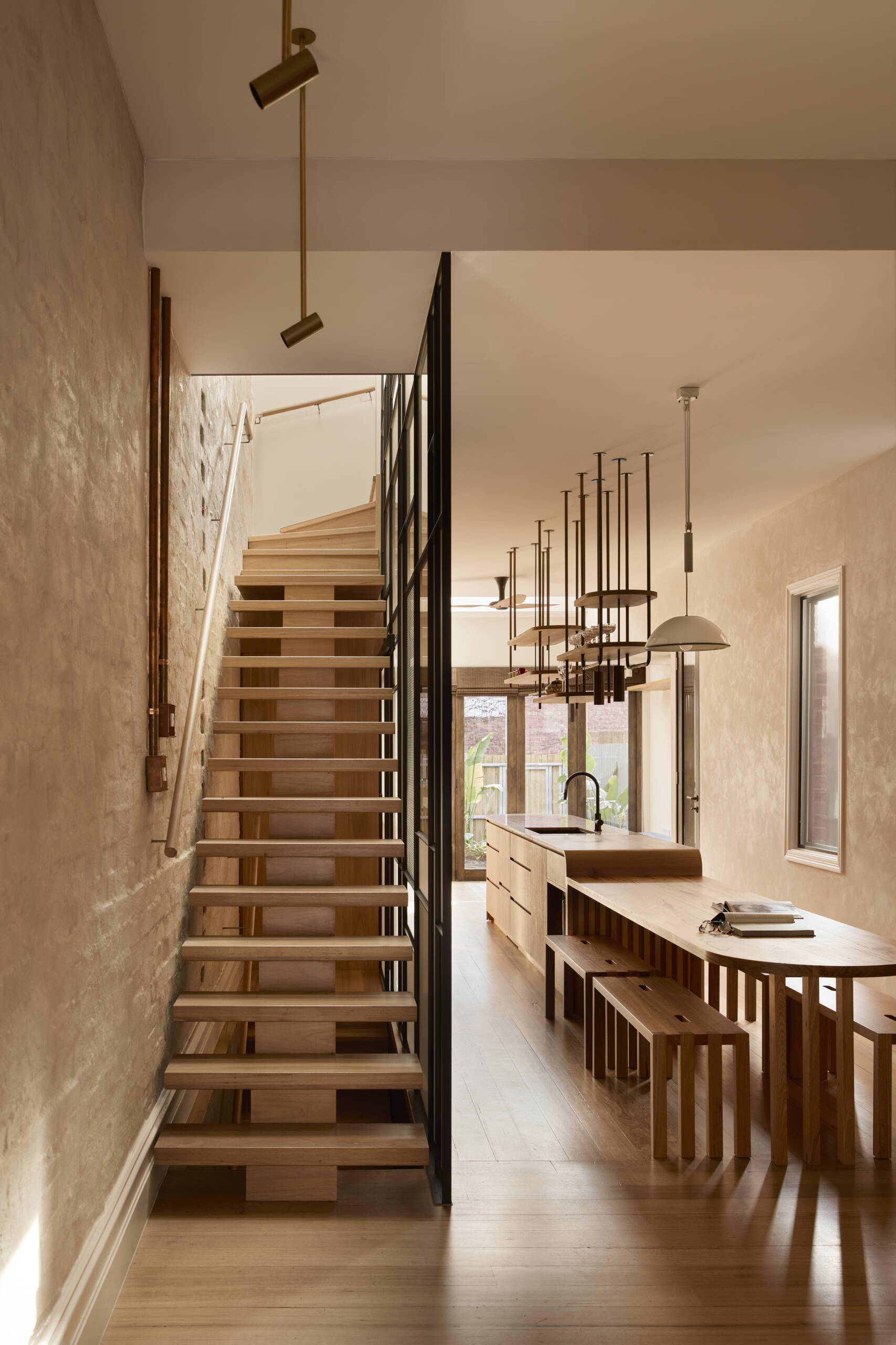 A sculptural floating staircase with glass balustrade and skylight above, bringing light into the centre of a terrace home.
