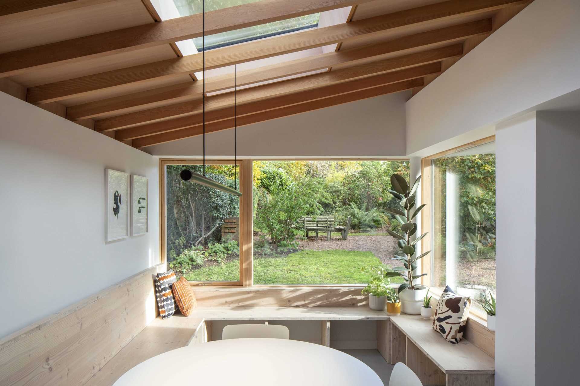 The standout feature of Origami House is its custom Douglas fir window seat. Wrapping around the extension in a generous U-shape, the built-in bench frames garden views, extends into the dining area, and continues toward the kitchen cabinetry.