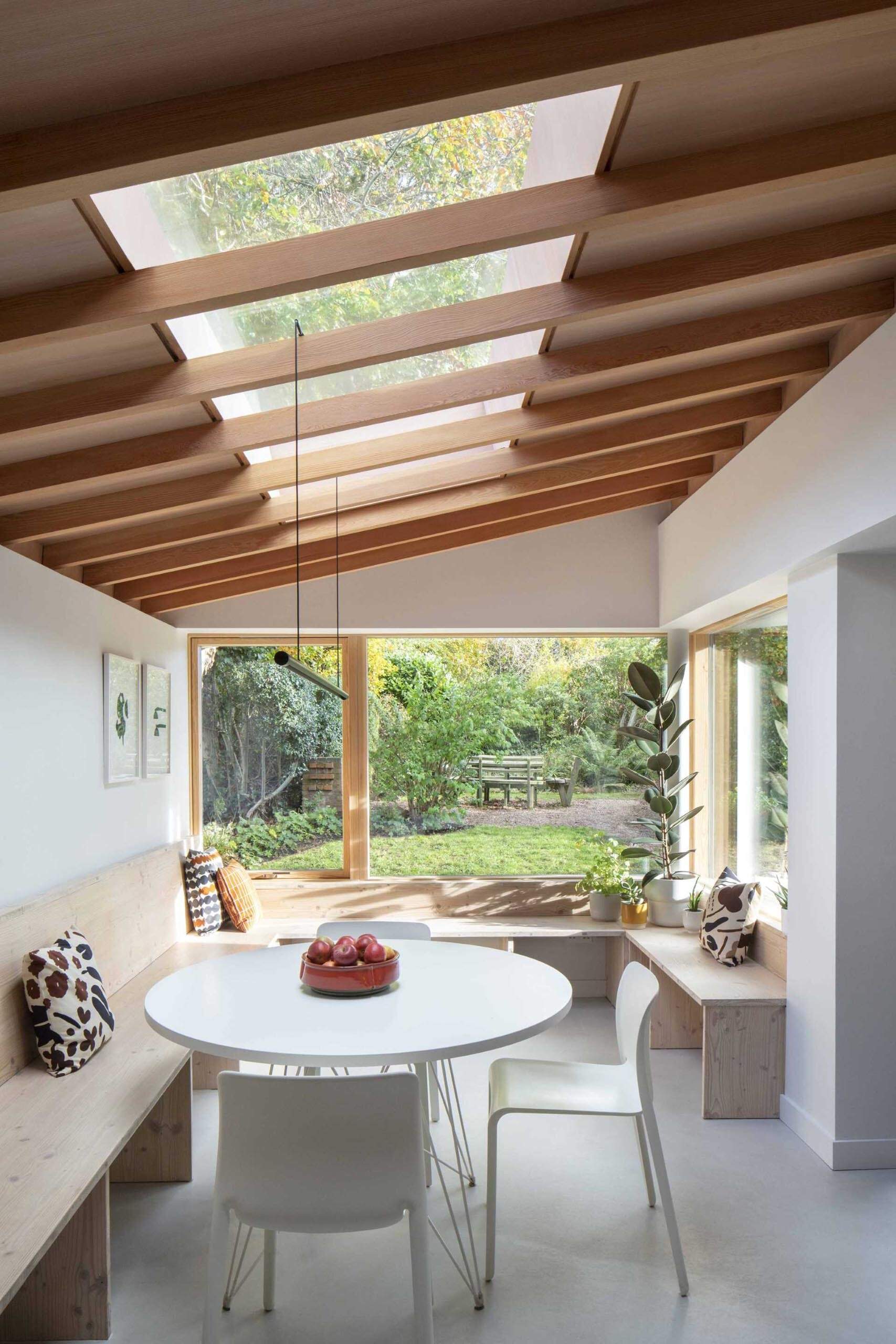 The standout feature of Origami House is its custom Douglas fir window seat. Wrapping around the extension in a generous U-shape, the built-in bench frames garden views, extends into the dining area, and continues toward the kitchen cabinetry.