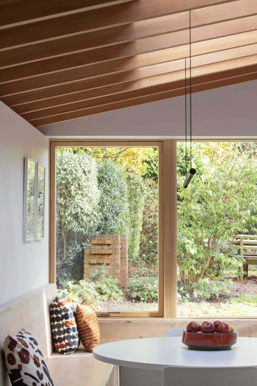 The standout feature of Origami House is its custom Douglas fir window seat. Wrapping around the extension in a generous U-shape, the built-in bench frames garden views, extends into the dining area, and continues toward the kitchen cabinetry.