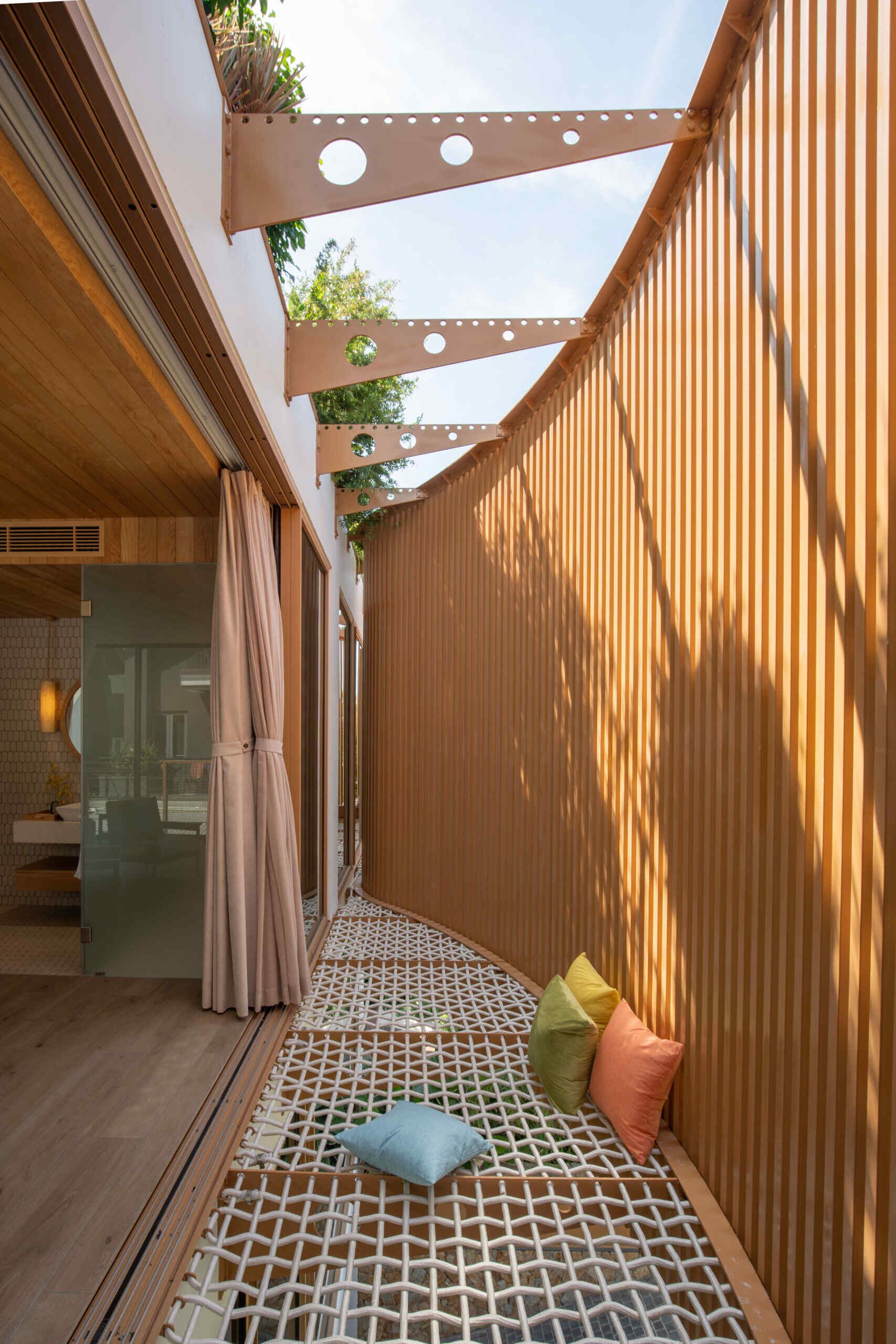 Warm timber finishes, a round soaking tub and a woven lounge net create a resort-inspired guest bedroom designed for relaxed coastal living.