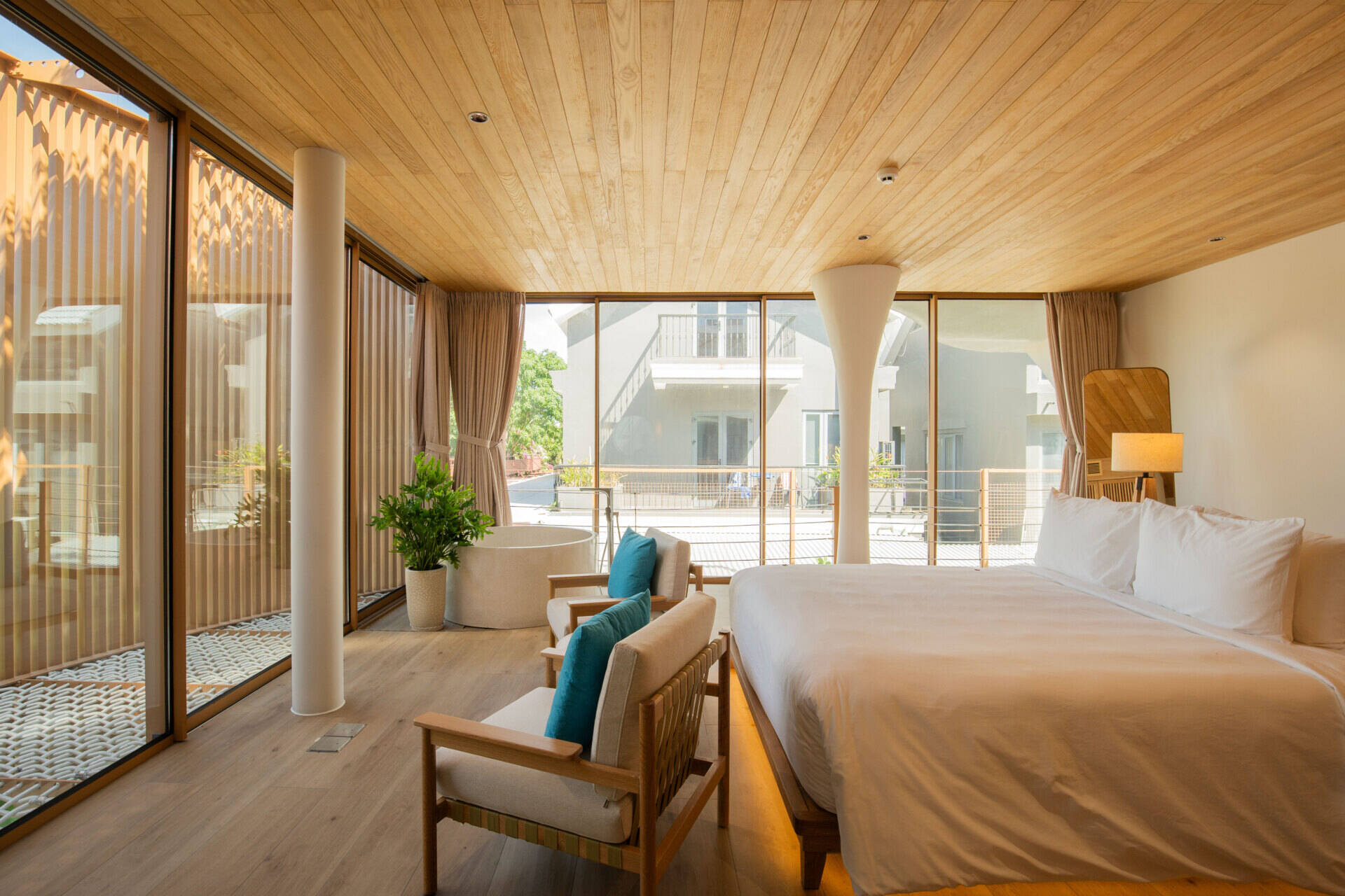 Warm timber finishes, a round soaking tub and a woven lounge net create a resort-inspired guest bedroom designed for relaxed coastal living.