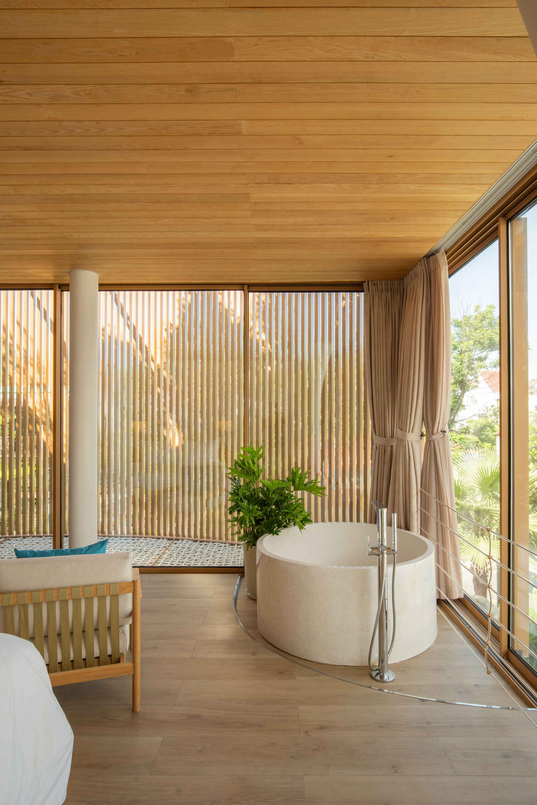 Warm timber finishes, a round soaking tub and a woven lounge net create a resort-inspired guest bedroom designed for relaxed coastal living.