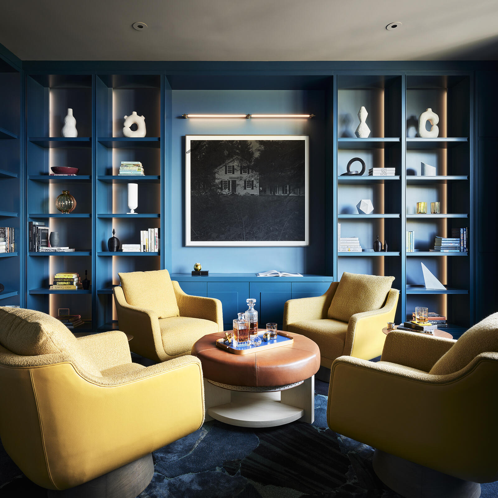 Wrapped in deep blue walls and custom shelving, this striking library proves that bold color can feel both sophisticated and inviting. Bright yellow seating, layered textures, and contemporary artwork create a cozy reading retreat with plenty of personality.