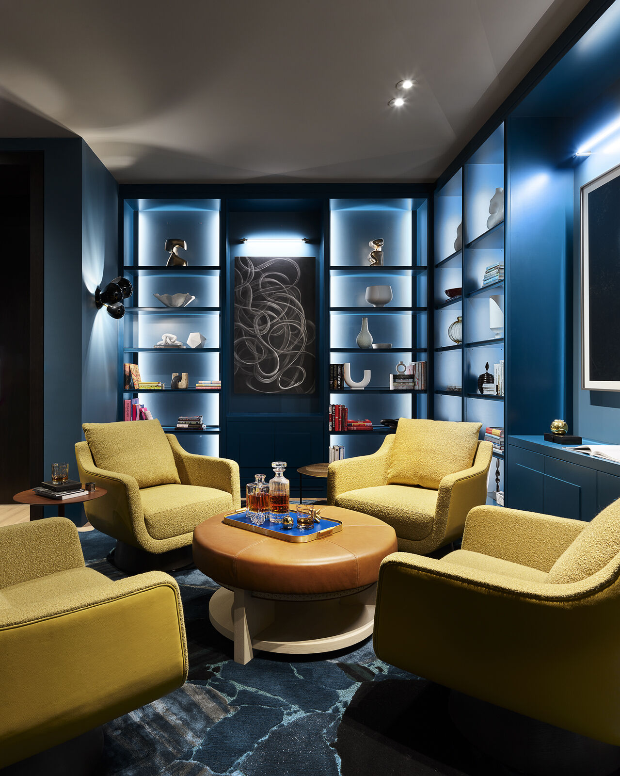 Wrapped in deep blue walls and custom shelving, this striking library proves that bold color can feel both sophisticated and inviting. Bright yellow seating, layered textures, and contemporary artwork create a cozy reading retreat with plenty of personality.