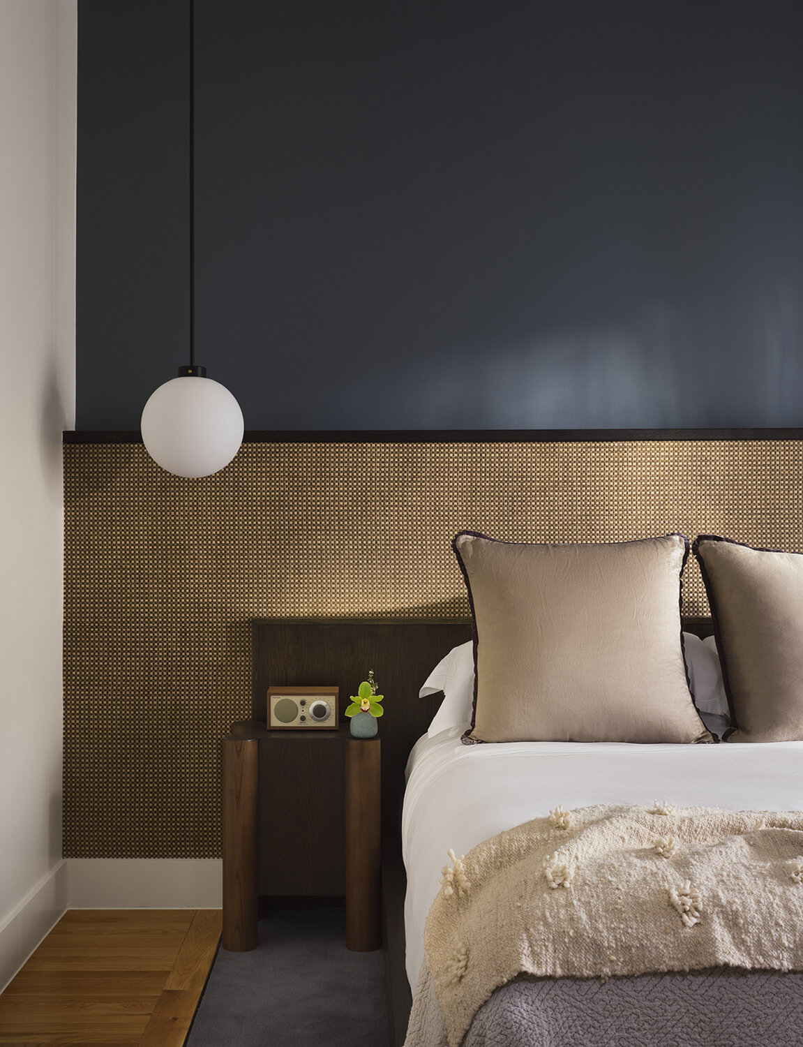 A modern hotel room with dusty blue walls and rattan accents.
