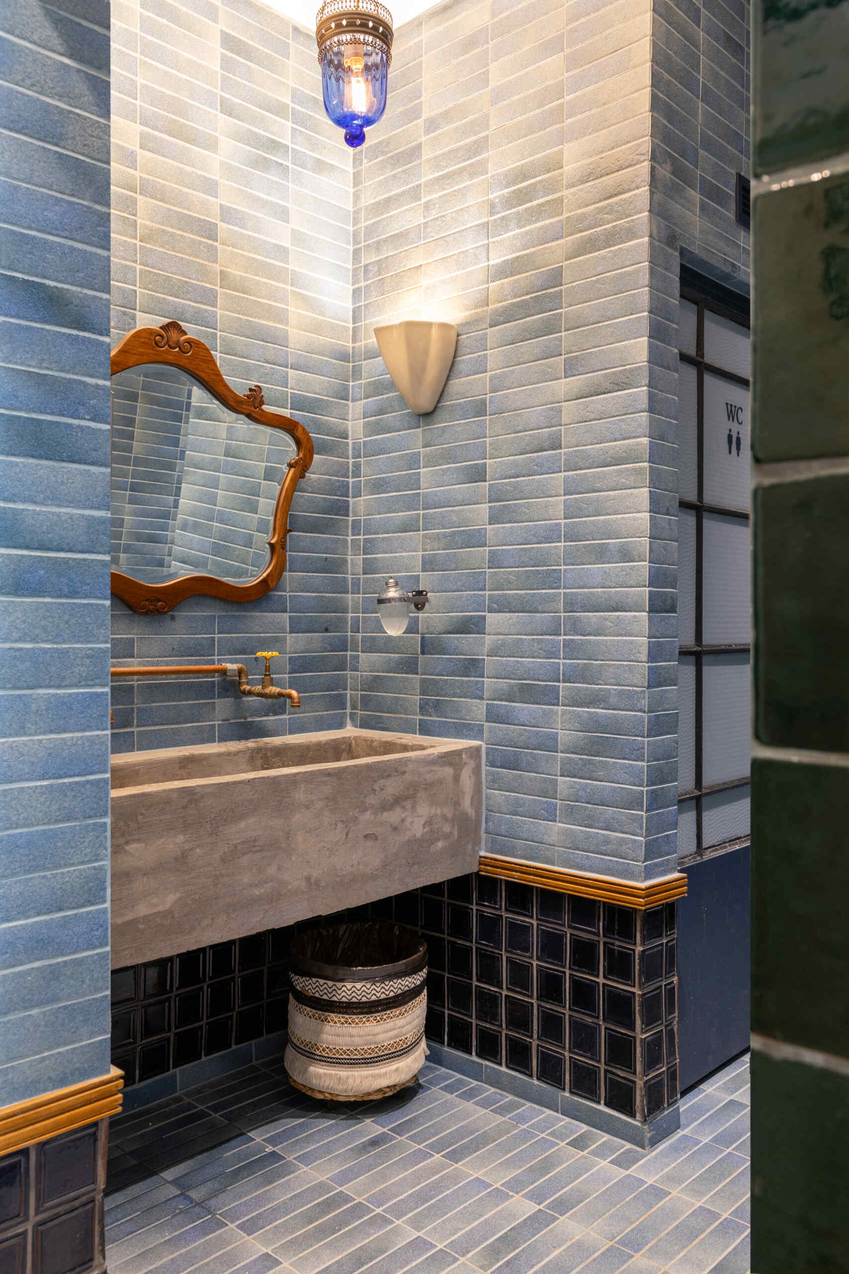 Blue and green ceramic tile panels, vintage mirrors, wooden detailing, and concrete sinks give the bathrooms the same architectural quality and material richness found throughout Casa Baruk.