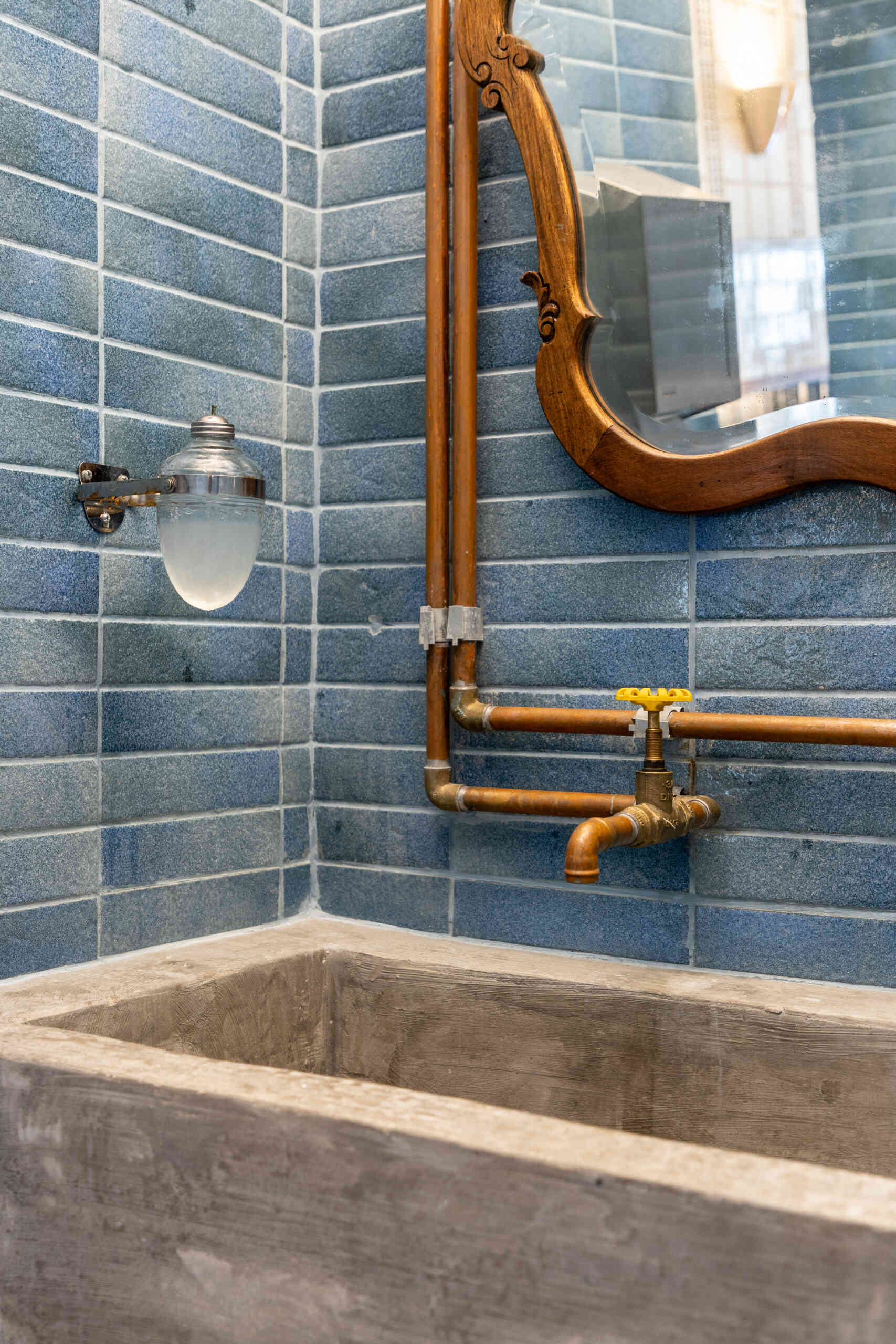 Blue and green ceramic tile panels, vintage mirrors, wooden detailing, and concrete sinks give the bathrooms the same architectural quality and material richness found throughout Casa Baruk.