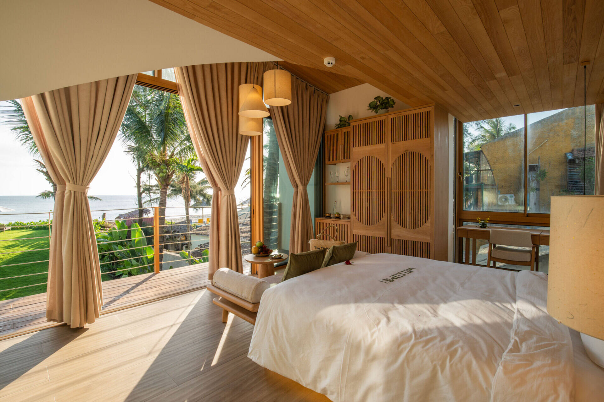 Sun-filled interiors, warm timber finishes and balcony views of palms and the water make this guest bedroom a calm coastal escape.