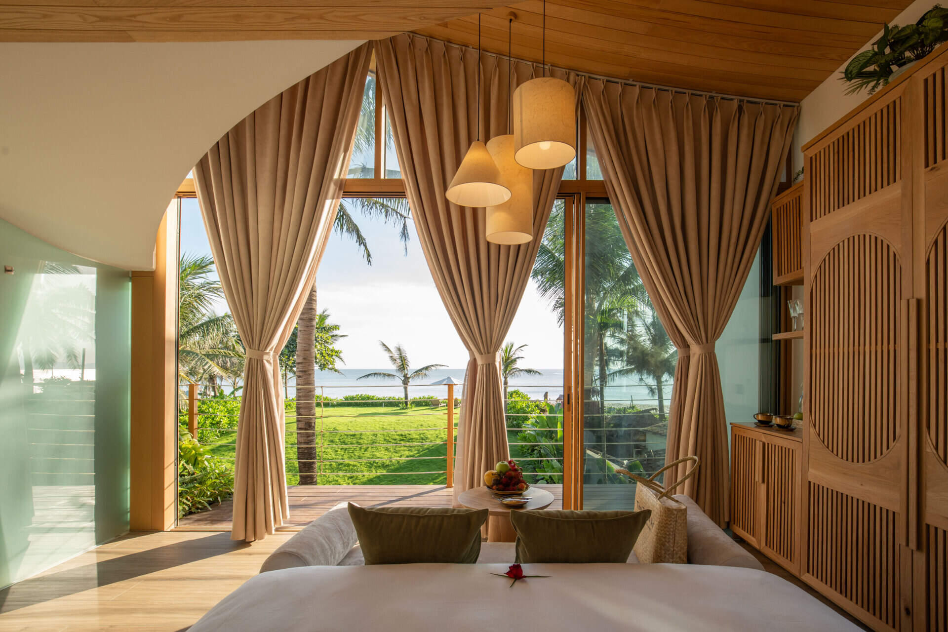 Sun-filled interiors, warm timber finishes and balcony views of palms and the water make this guest bedroom a calm coastal escape.