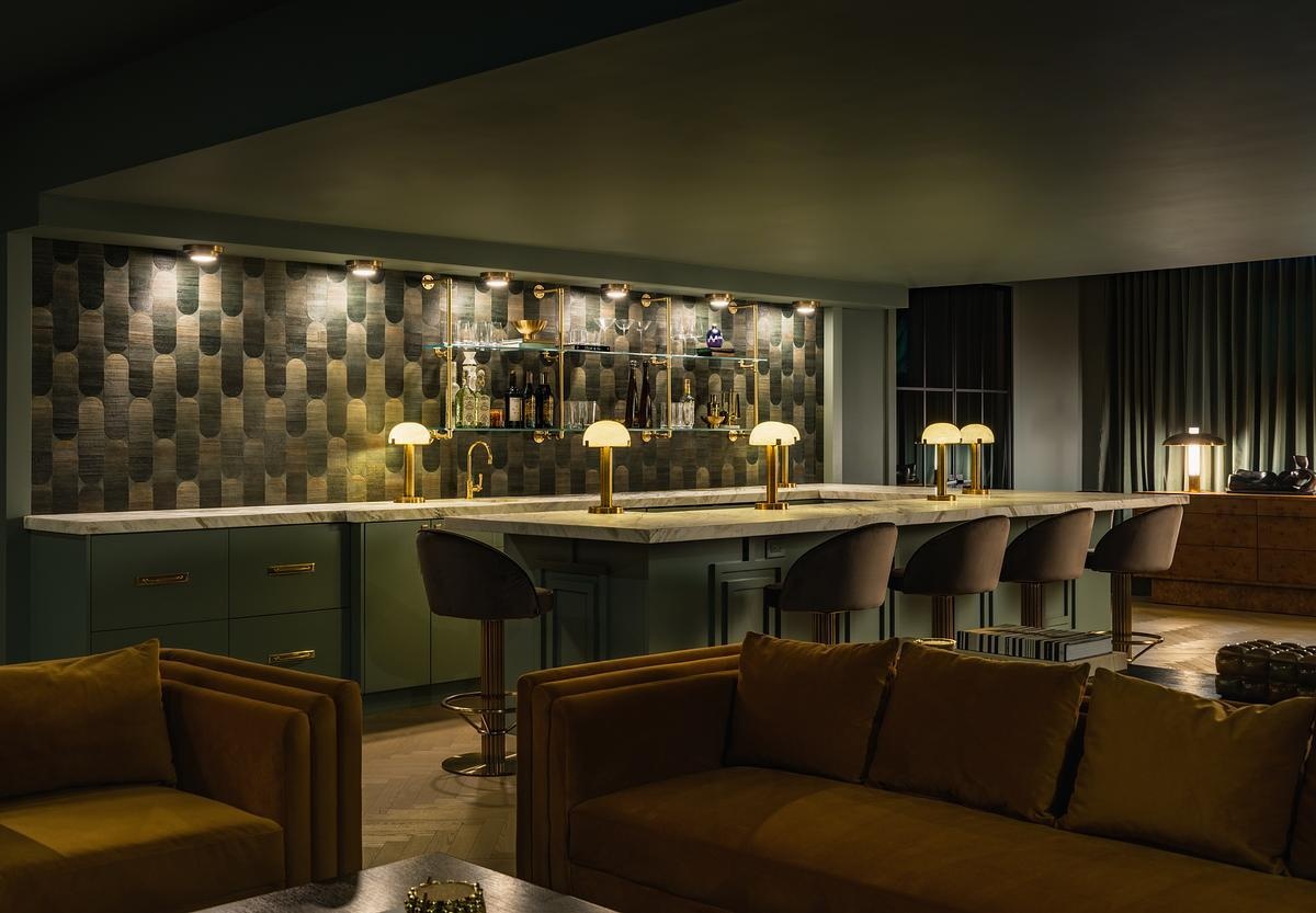 This speakeasy-inspired home whiskey lounge features rich green cabinetry, South African marble, brass accents, velvet seating, and vintage-inspired details.