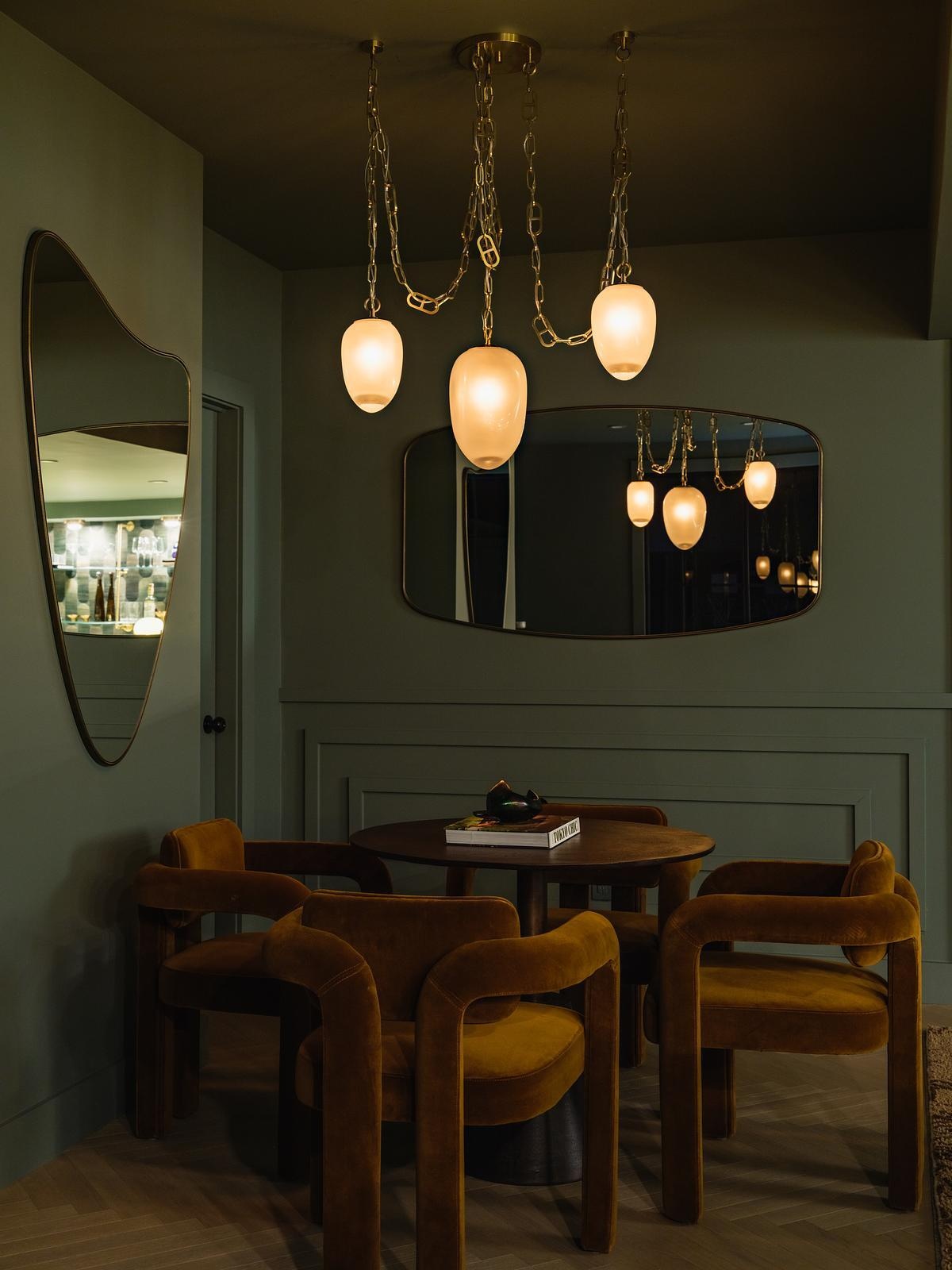 This speakeasy-inspired home whiskey lounge features rich green cabinetry, South African marble, brass accents, velvet seating, and vintage-inspired details.