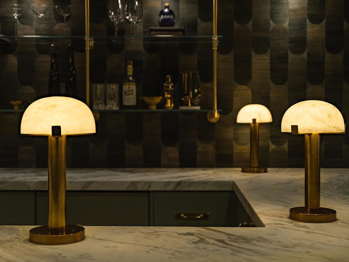 This speakeasy-inspired home whiskey lounge features rich green cabinetry, South African marble, brass accents, velvet seating, and vintage-inspired details.