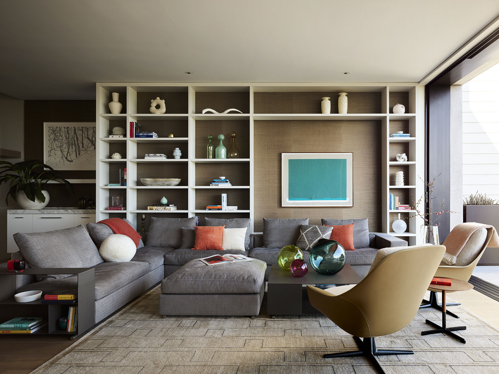 Centered around a custom bookcase filled with travel finds and personal treasures, this welcoming family room blends contemporary design with everyday comfort. A vibrant artwork by Analia Saban, textured finishes, and relaxed seating create a space designed for gathering, unwinding, and making memories.
