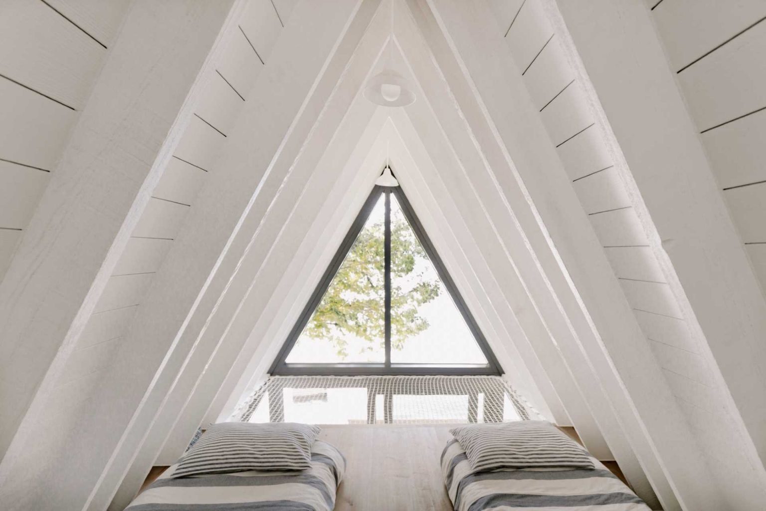 Tucked beneath the dramatic A-frame roof, this loft bedroom combines cozy sleeping quarters with beautiful lake views and a unique reading net above the living room.