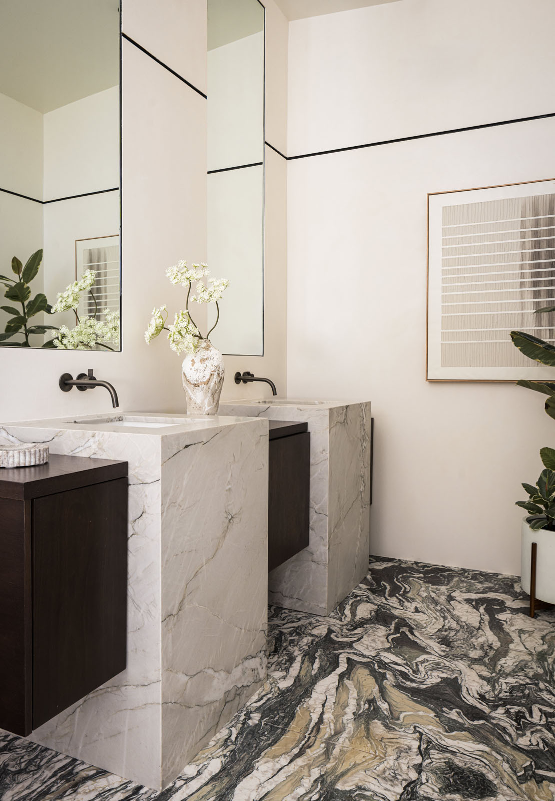 Bold veined stone, sculptural vanities, and a freestanding bath beside a tree-filled window give this primary bathroom the feel of a luxurious spa.