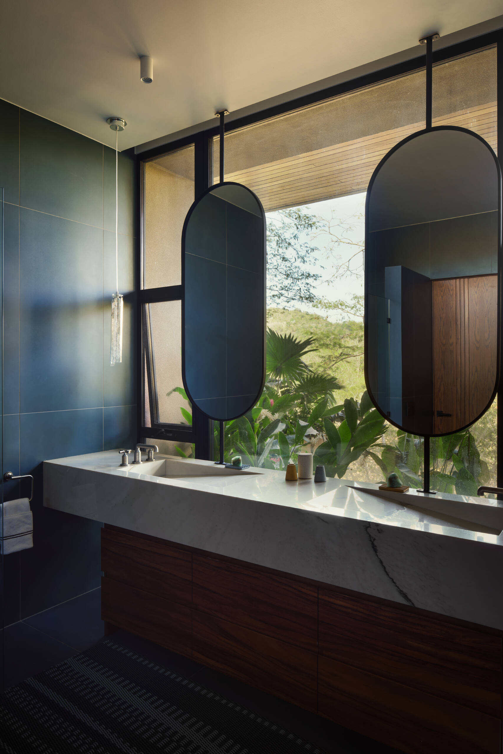 Rich stone, warm timber, textured tiles, and generous natural light give these bathrooms a relaxed contemporary feel.
