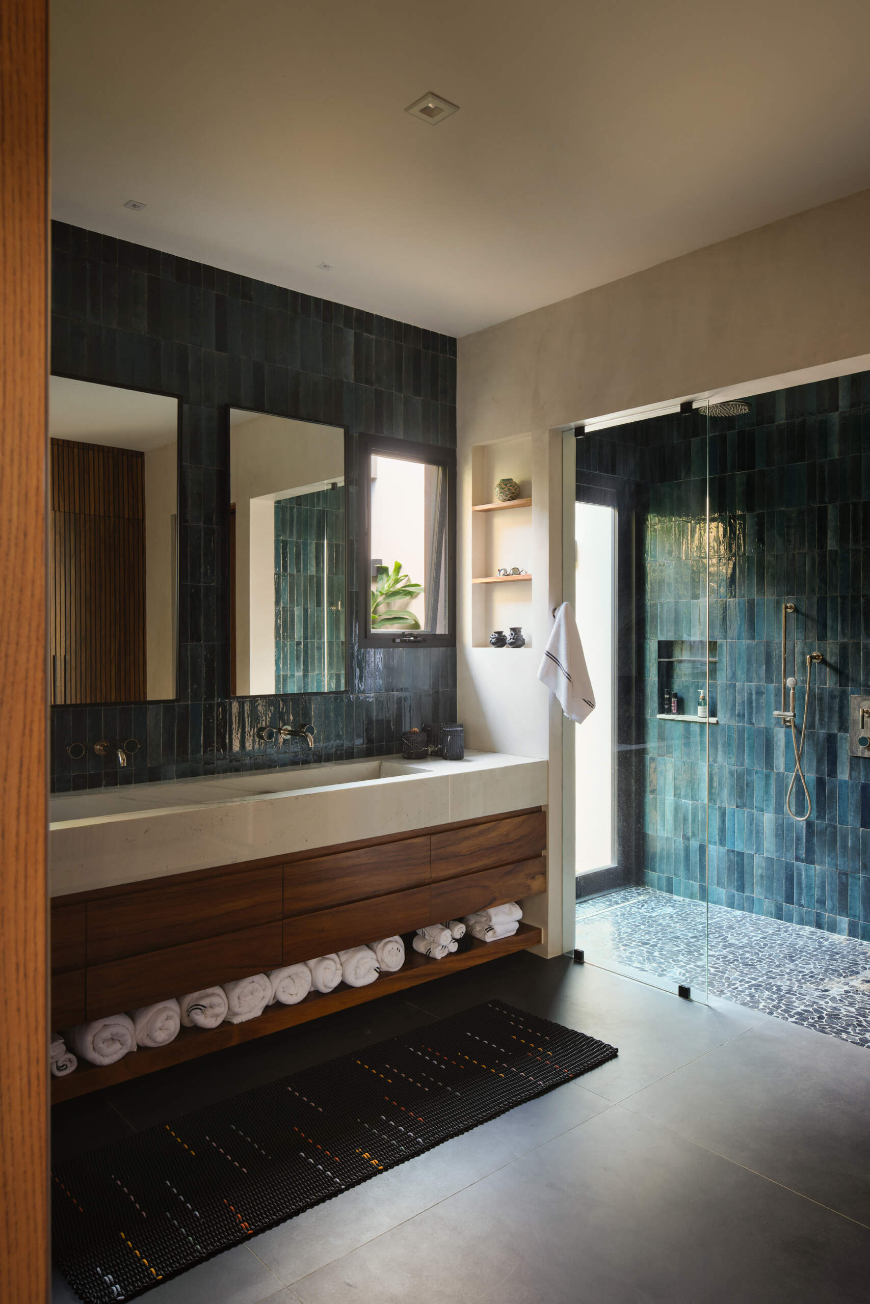 Rich stone, warm timber, textured tiles, and generous natural light give these bathrooms a relaxed contemporary feel.