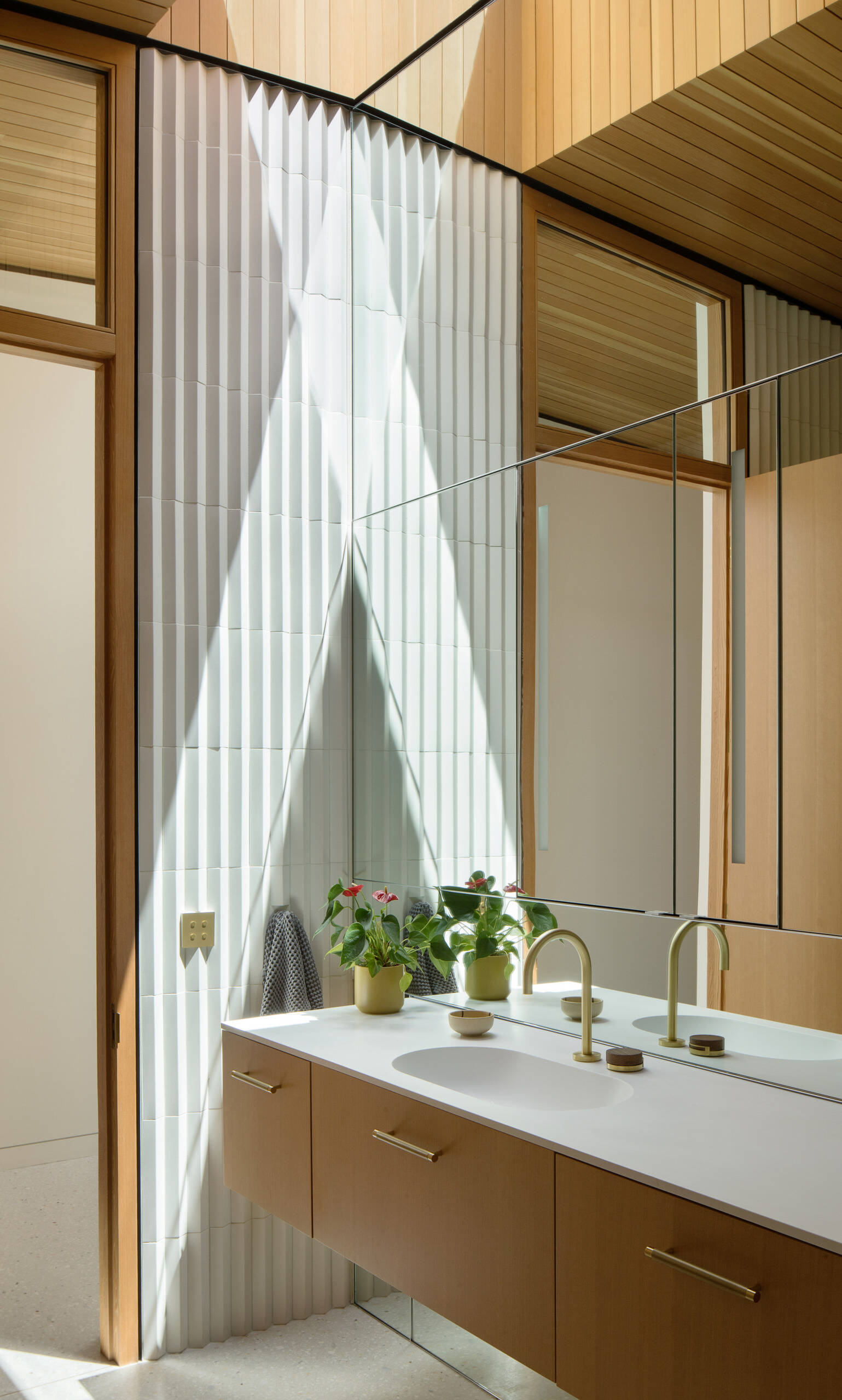 El baño de visitas combina maderas cálidas, azulejos texturizados, accesorios de latón y una hermosa luz natural para crear una apariencia fresca y moderna.