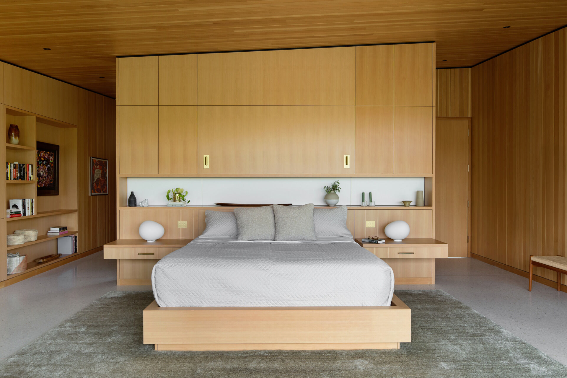 Ingrese a un cálido dormitorio de madera con almacenamiento incorporado, carpintería de piso a techo y tonos relajantes diseñados para brindar comodidad y simplicidad.