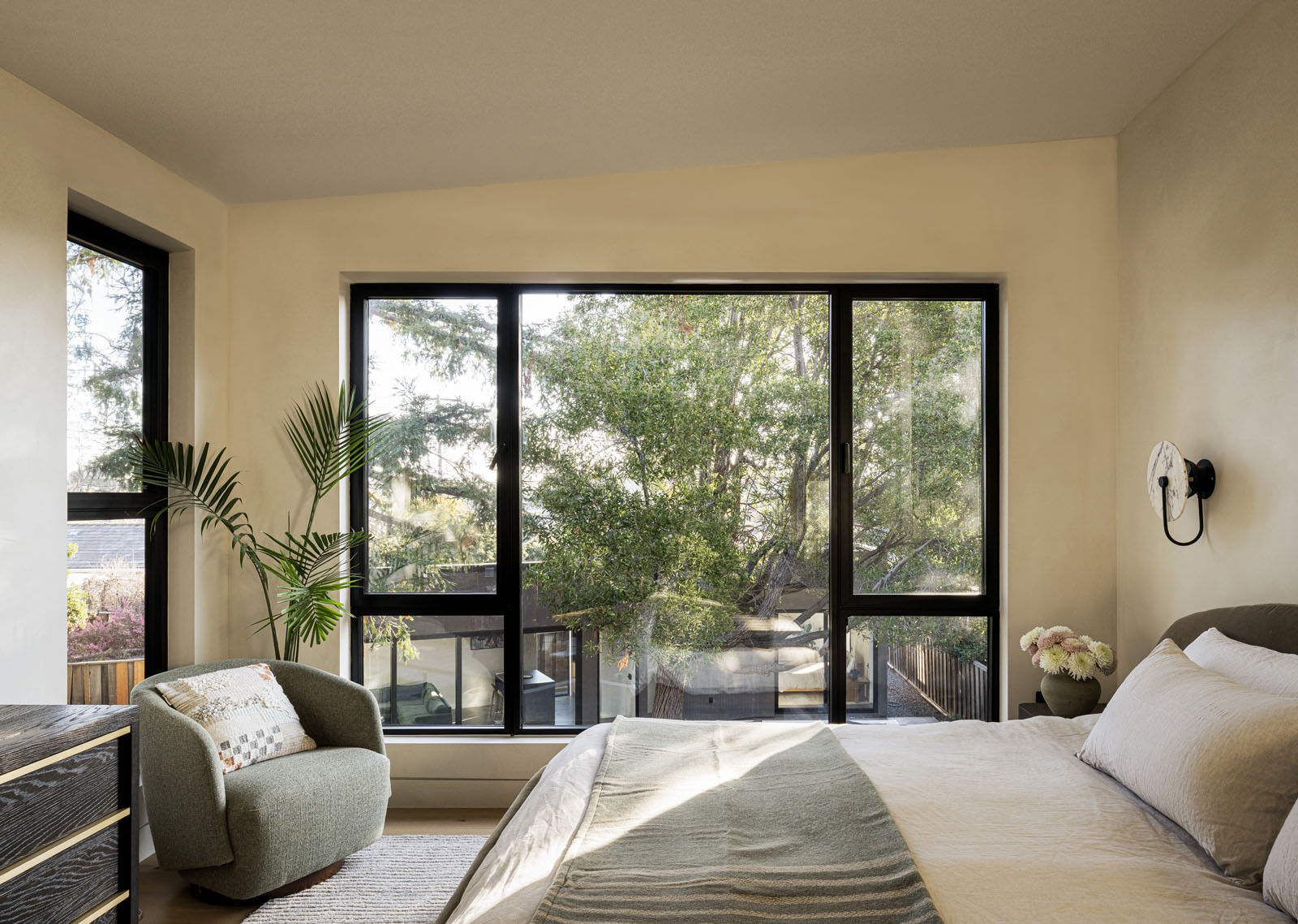 Wake up to tree-filled views in this serene primary bedroom, where floor-to-ceiling glazing and soft neutral finishes create a bright, calming atmosphere.