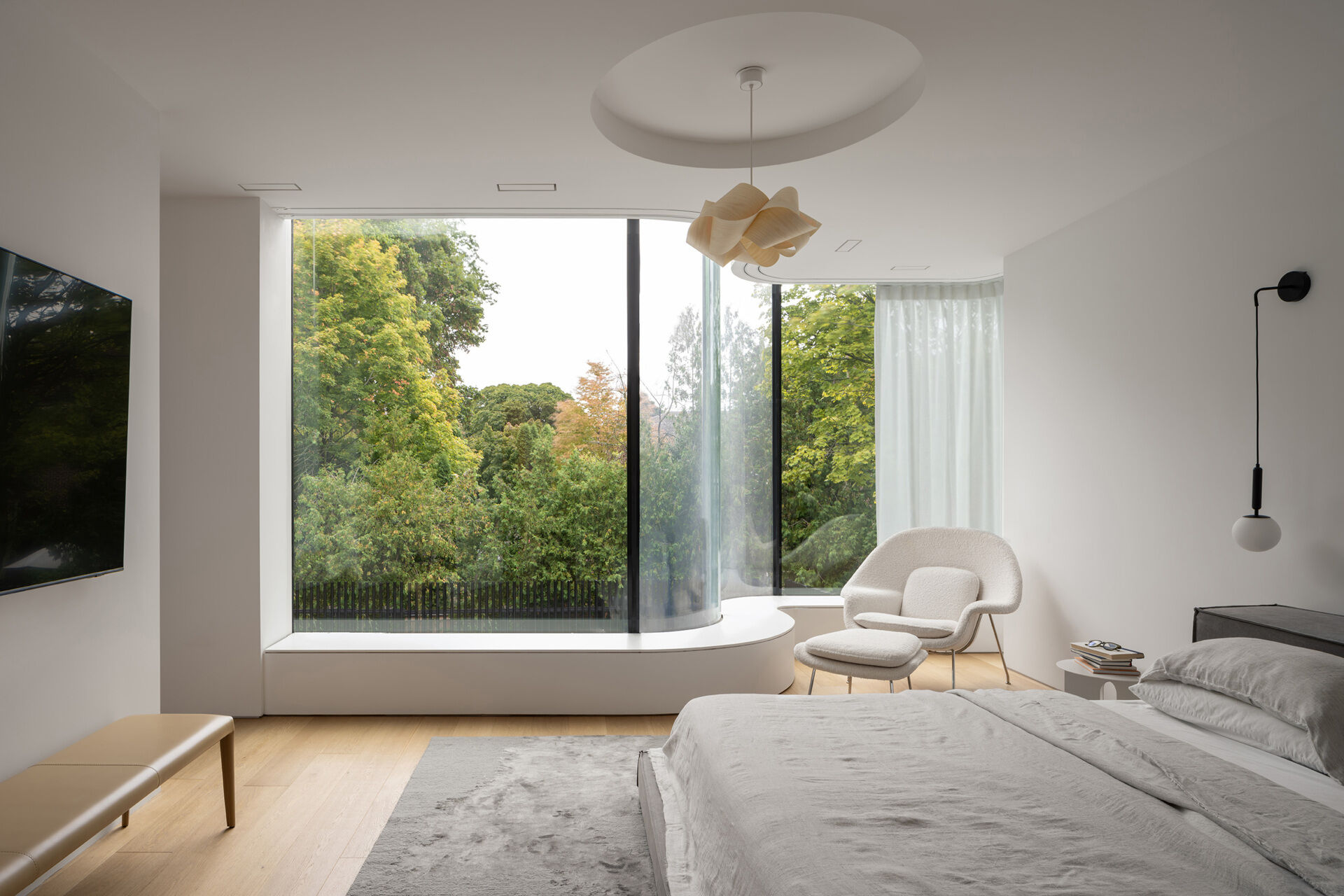 The primary bedroom in the curved glass addition feels light-filled and private, with soft furnishings and treetop views.
