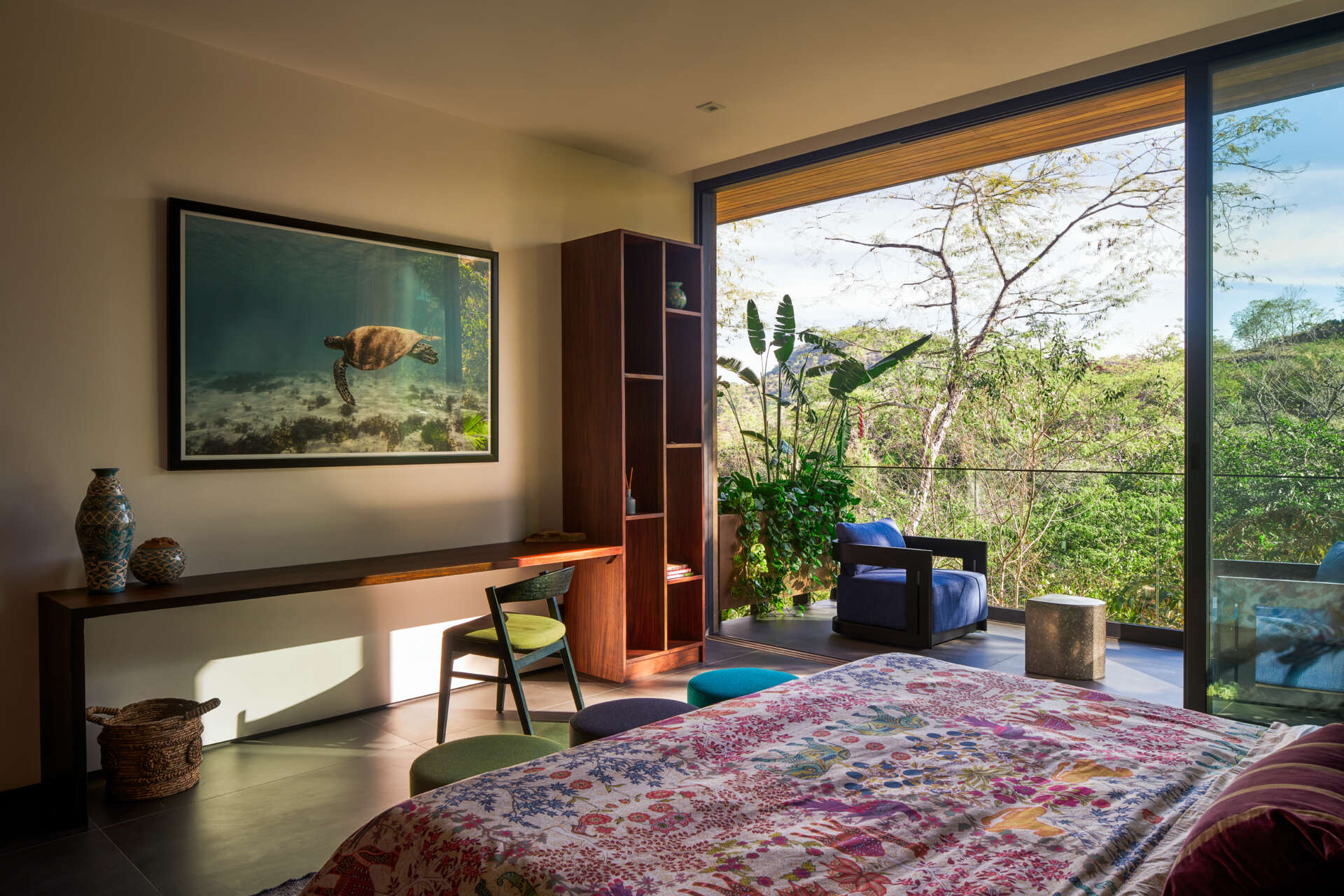 This bright bedroom at Casa Akíga combines colourful textiles, custom timber furniture, a private balcony, and expansive jungle views to create a relaxed tropical escape.