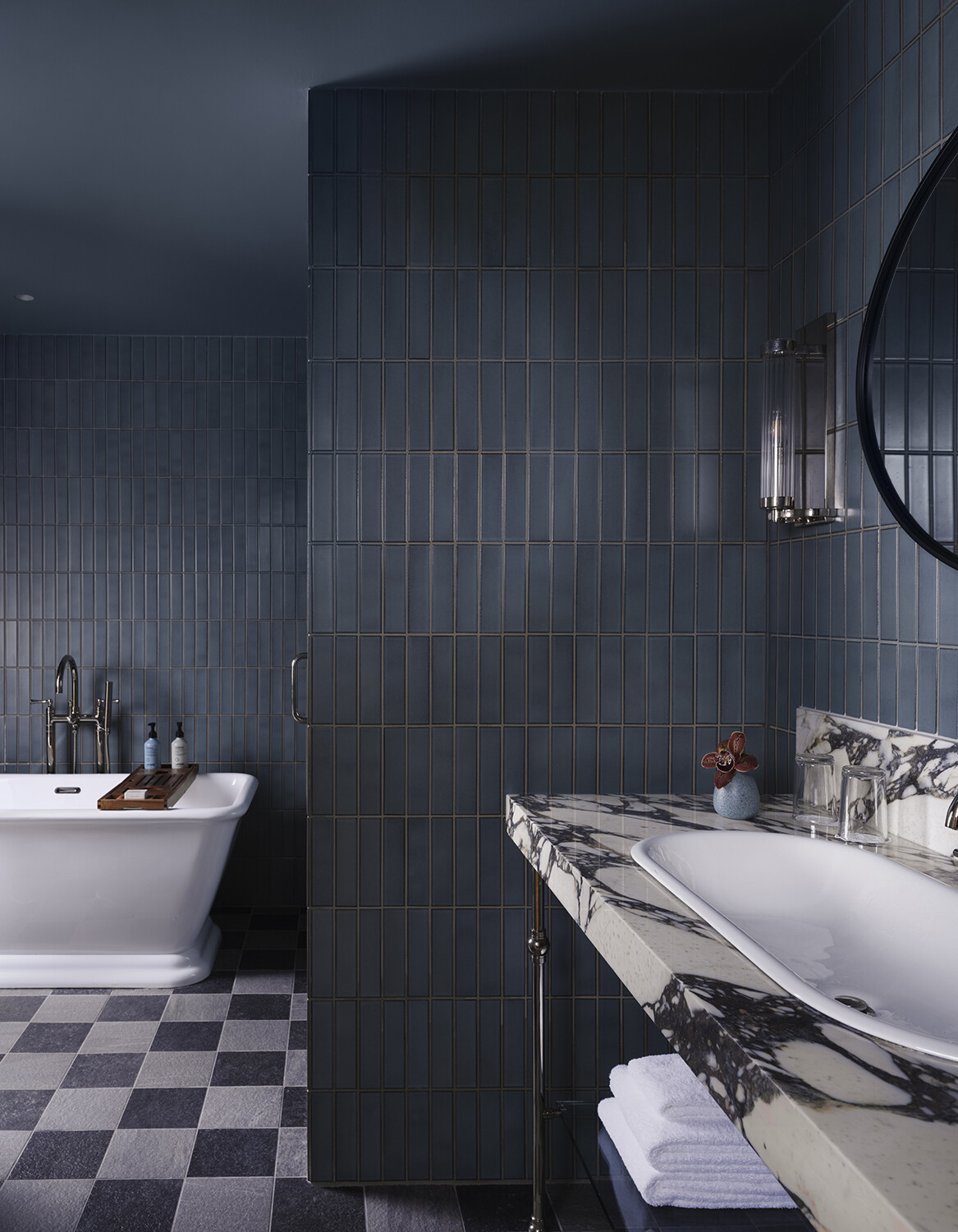 A modern bathroom with a marble vanity, vertical deep blue tiles covering the walls, and checkerboard flooring.