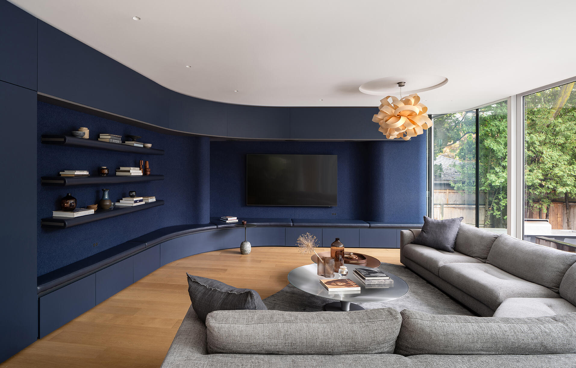 A cozy blue family room with felt-lined cabinetry, curved walls, and a garden connection inside the new glass addition.