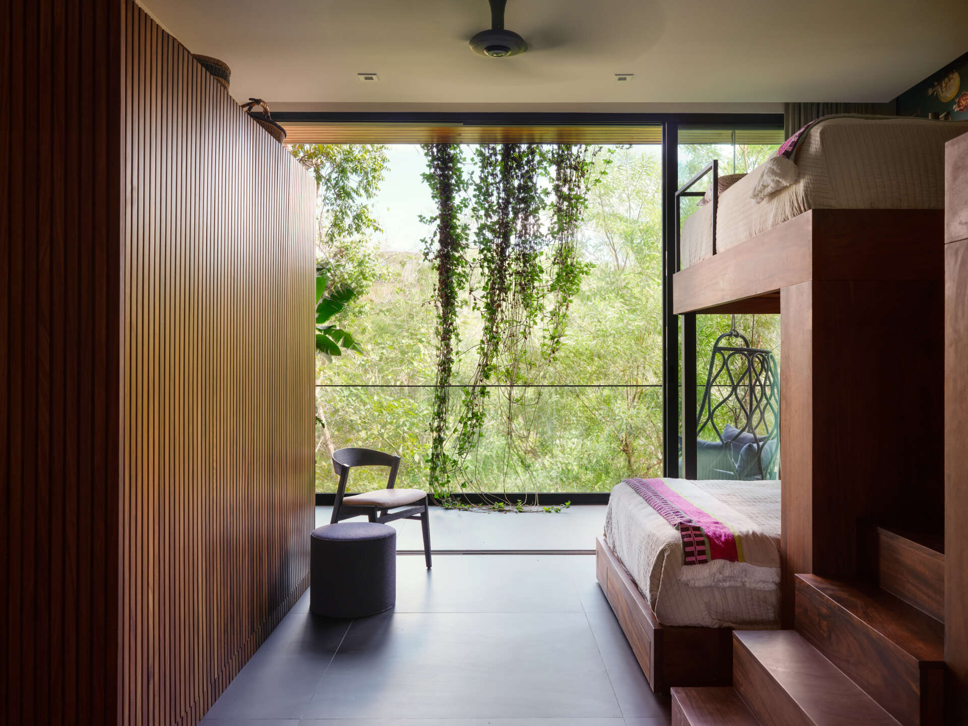 This custom bunk room at Casa Akíga combines warm timber joinery, built-in storage, a playful feature wall, and jungle views to create a space that's both practical and inviting.