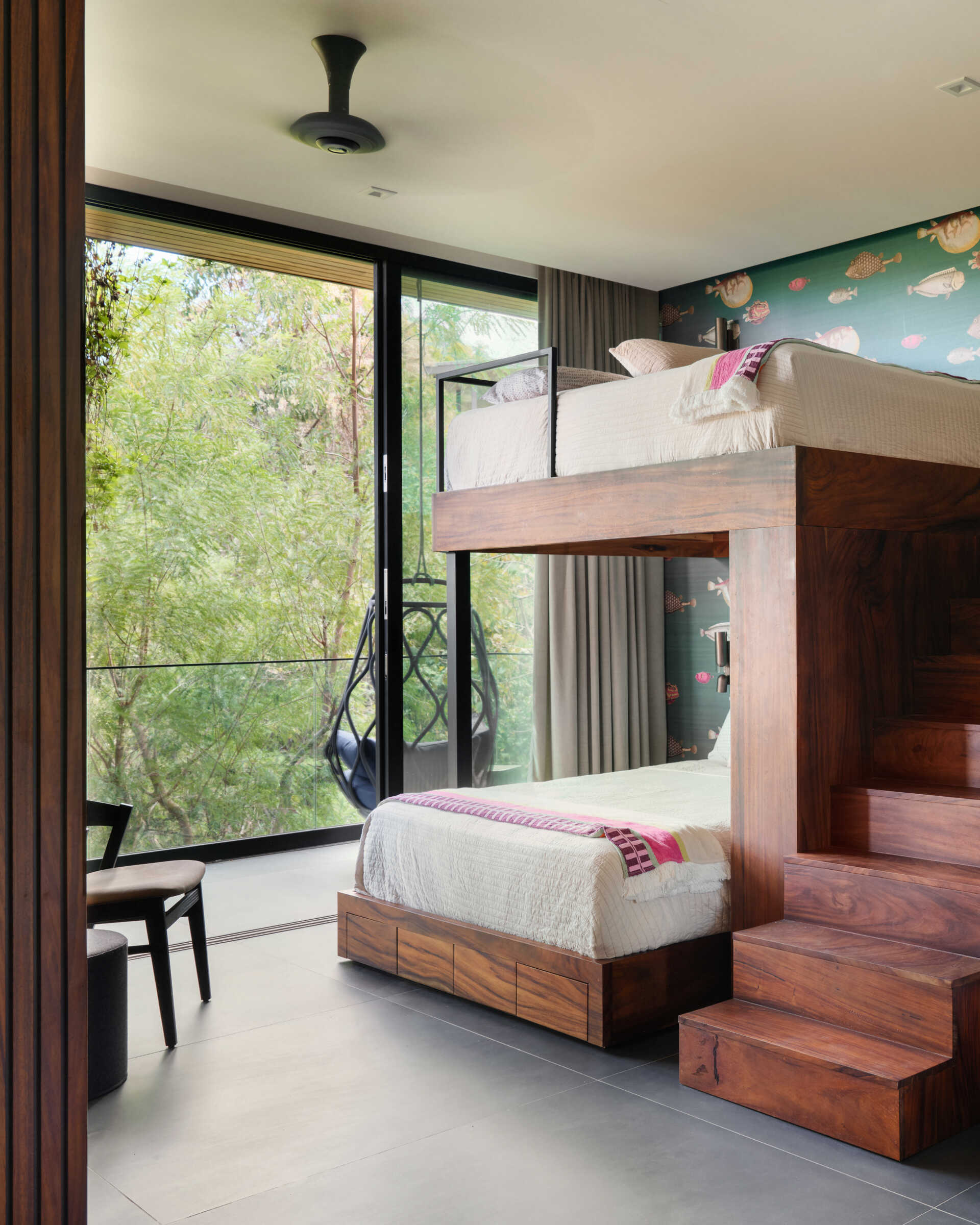 This custom bunk room at Casa Akíga combines warm timber joinery, built-in storage, a playful feature wall, and jungle views to create a space that's both practical and inviting.