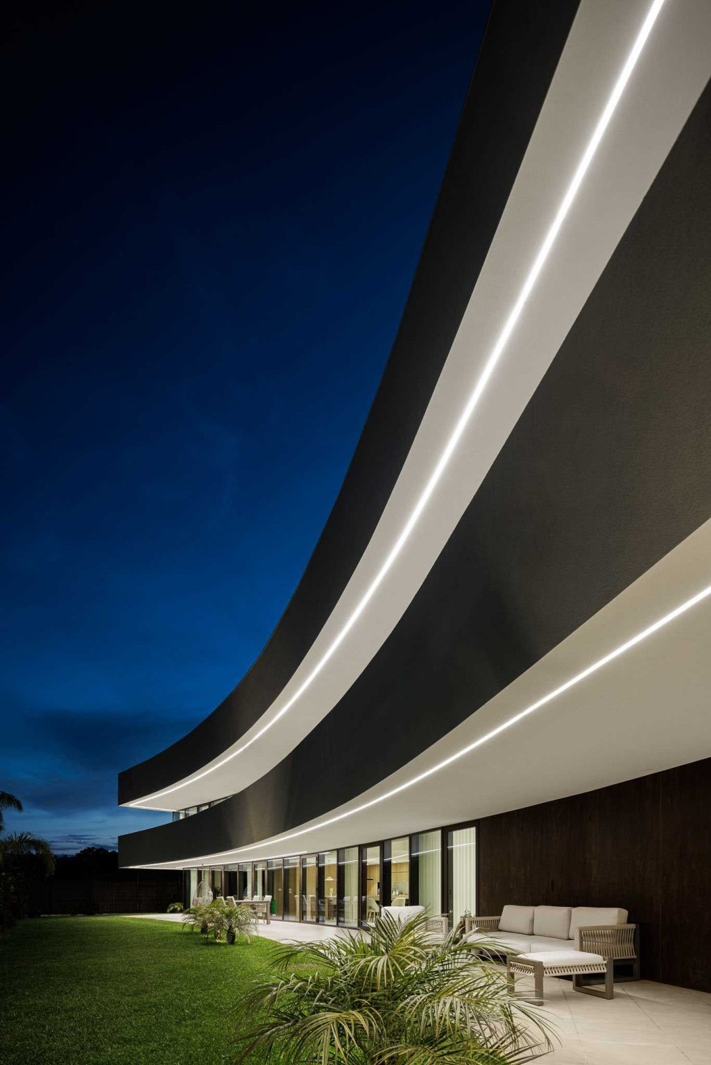 Integrated exterior lighting highlights the home's sweeping architecture after sunset, revealing the elegant curve from an entirely new perspective.